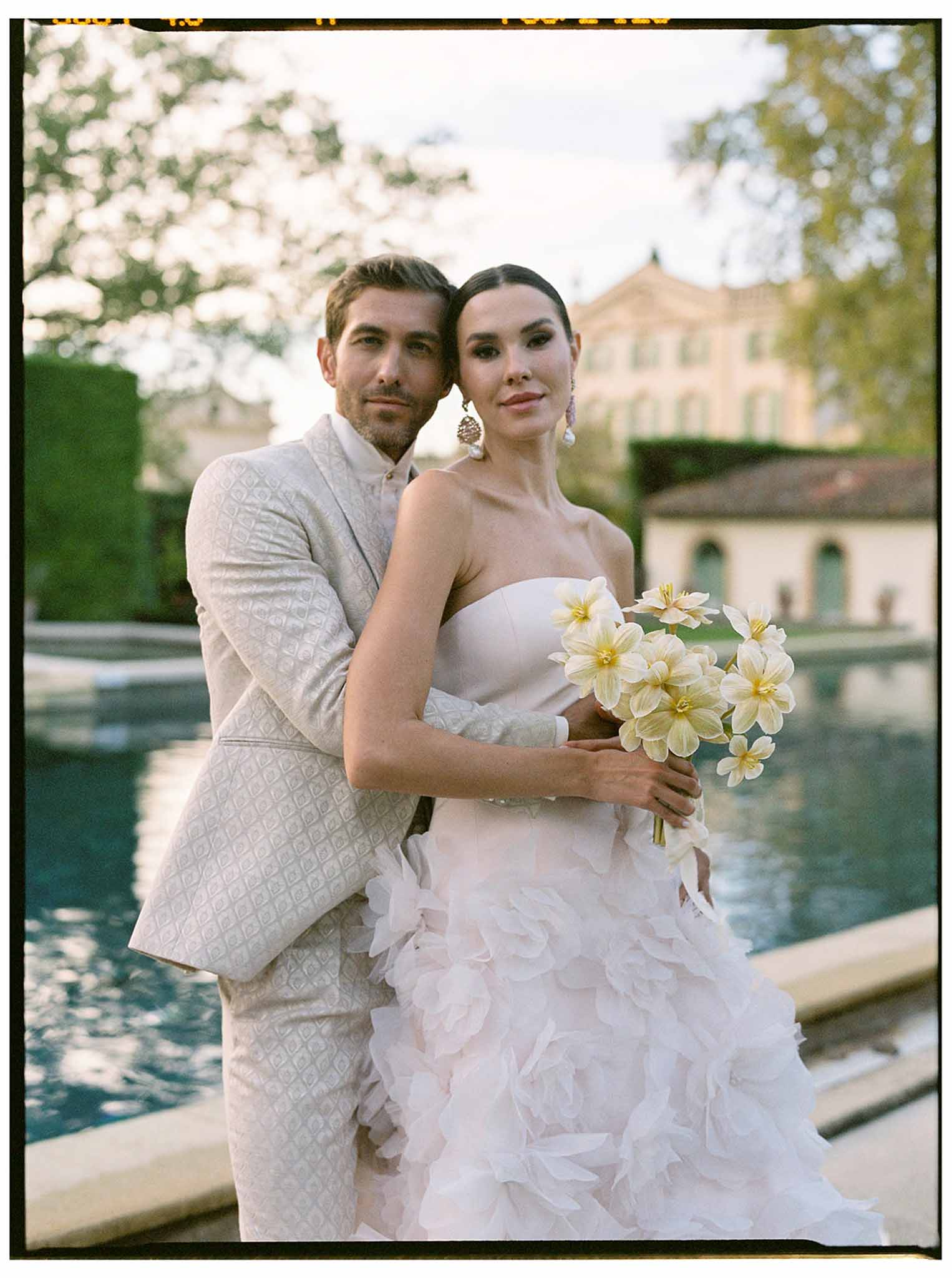 Bride and groom formal portrait beside reflecting pool at classical estate with historic stone building