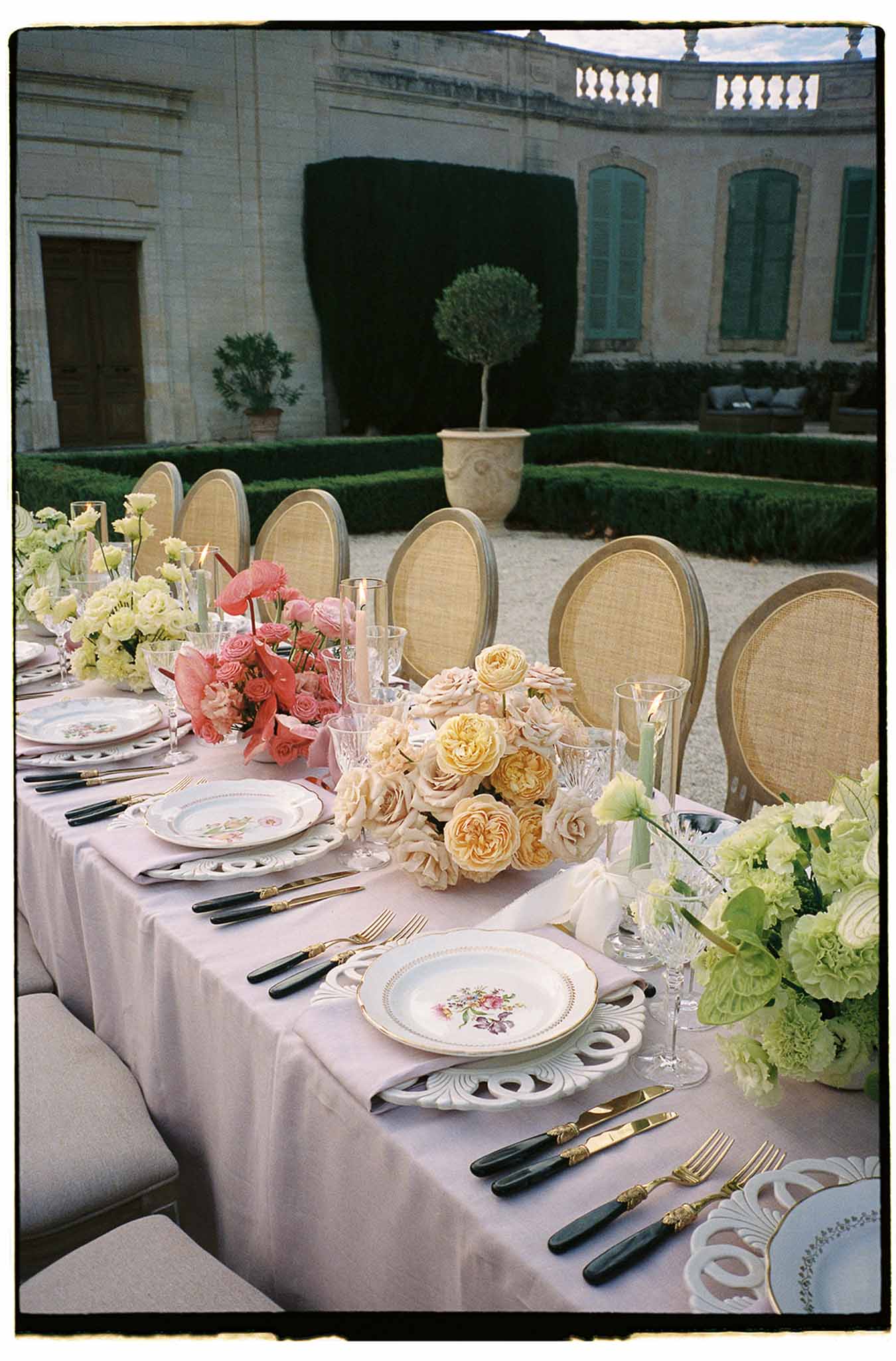 Formal reception table setting with pink linens and coral floral centerpieces in classical château courtyard