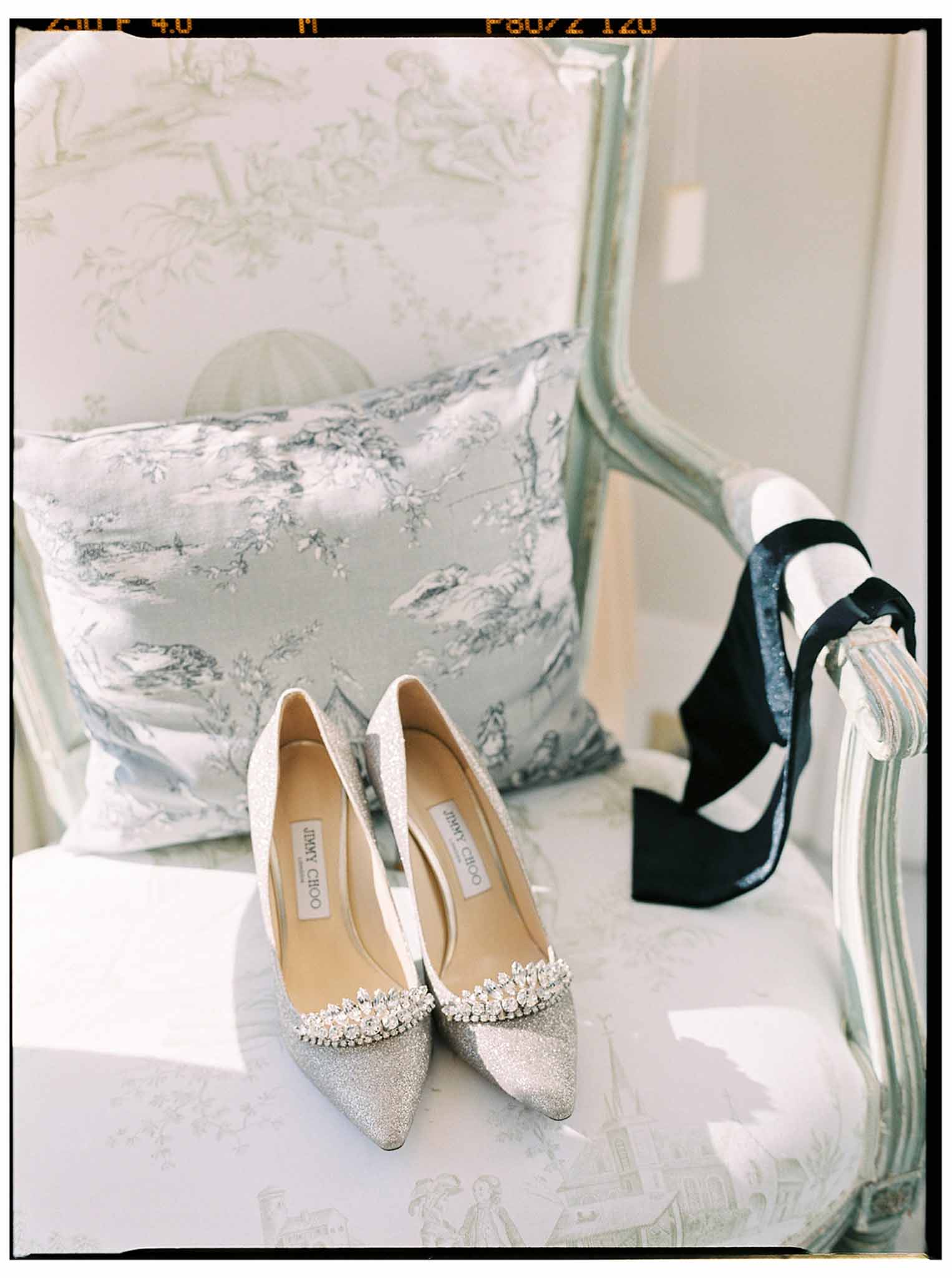 Ivory Jimmy Choo wedding shoes with crystal details arranged on bed with decorative pillows