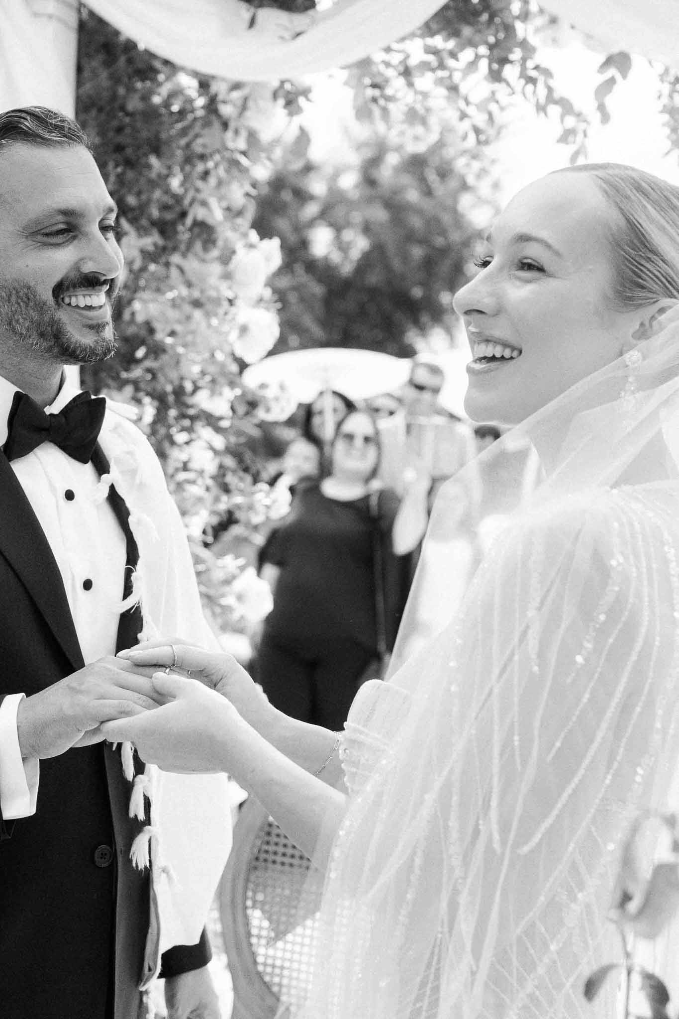 Couple exchanging rings during outdoor garden ceremony under white floral canopy