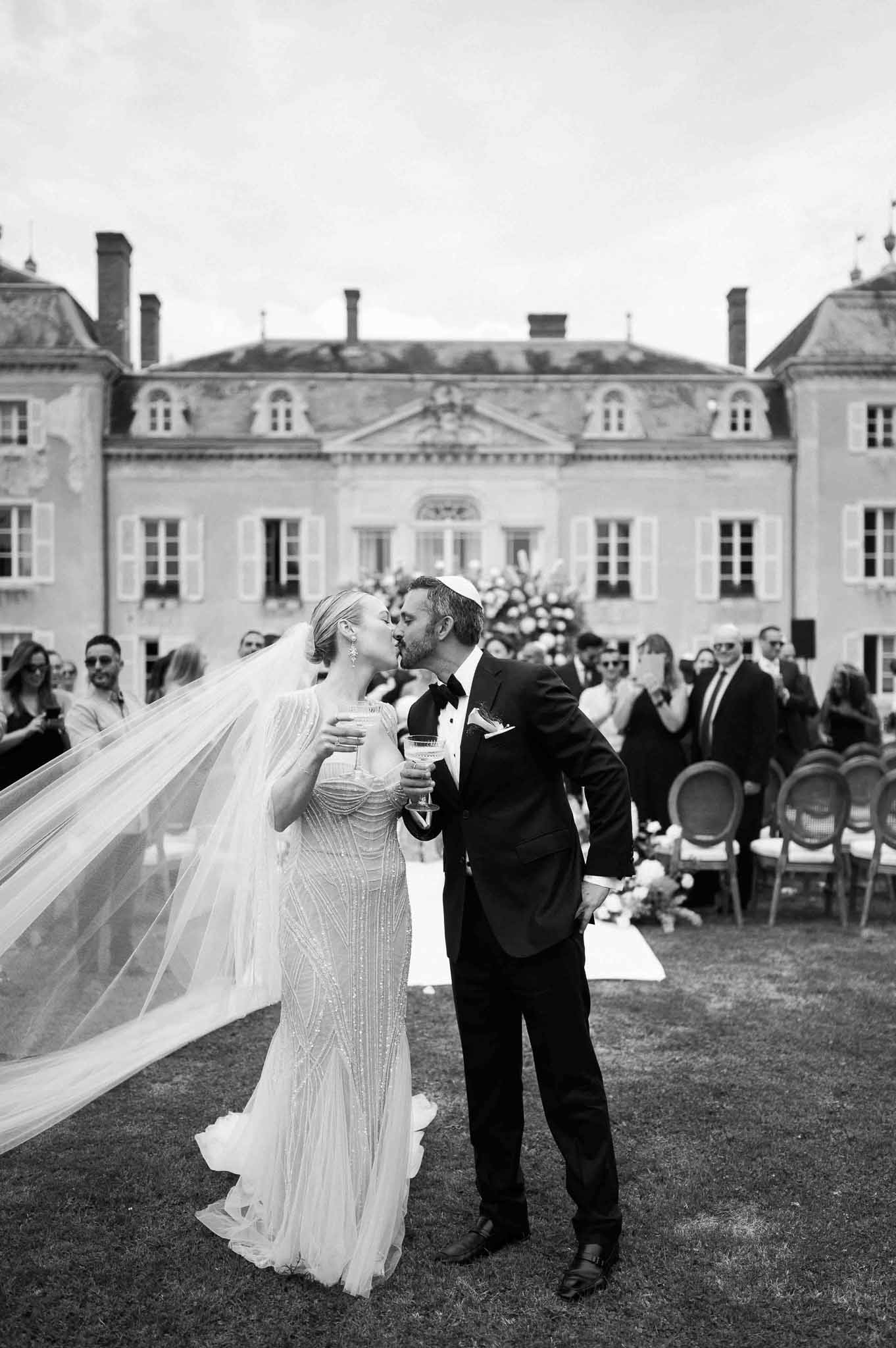 Newlyweds first kiss during ceremony recessional at French château with guests and classical architecture