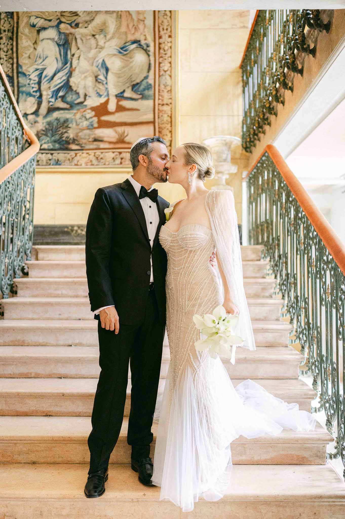 Bride and groom kissing on grand staircase in classical château interior