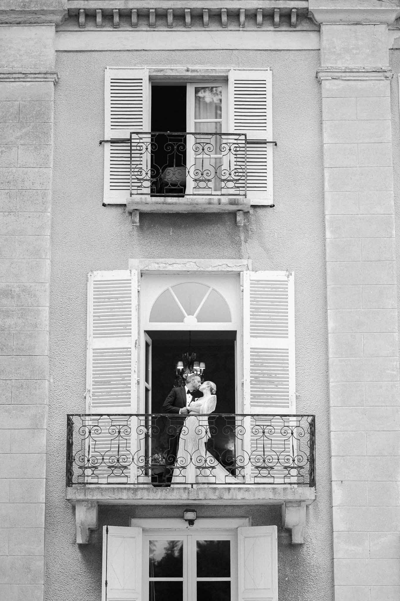 Bride and groom on ornate wrought-iron balcony at classical stone facade venue