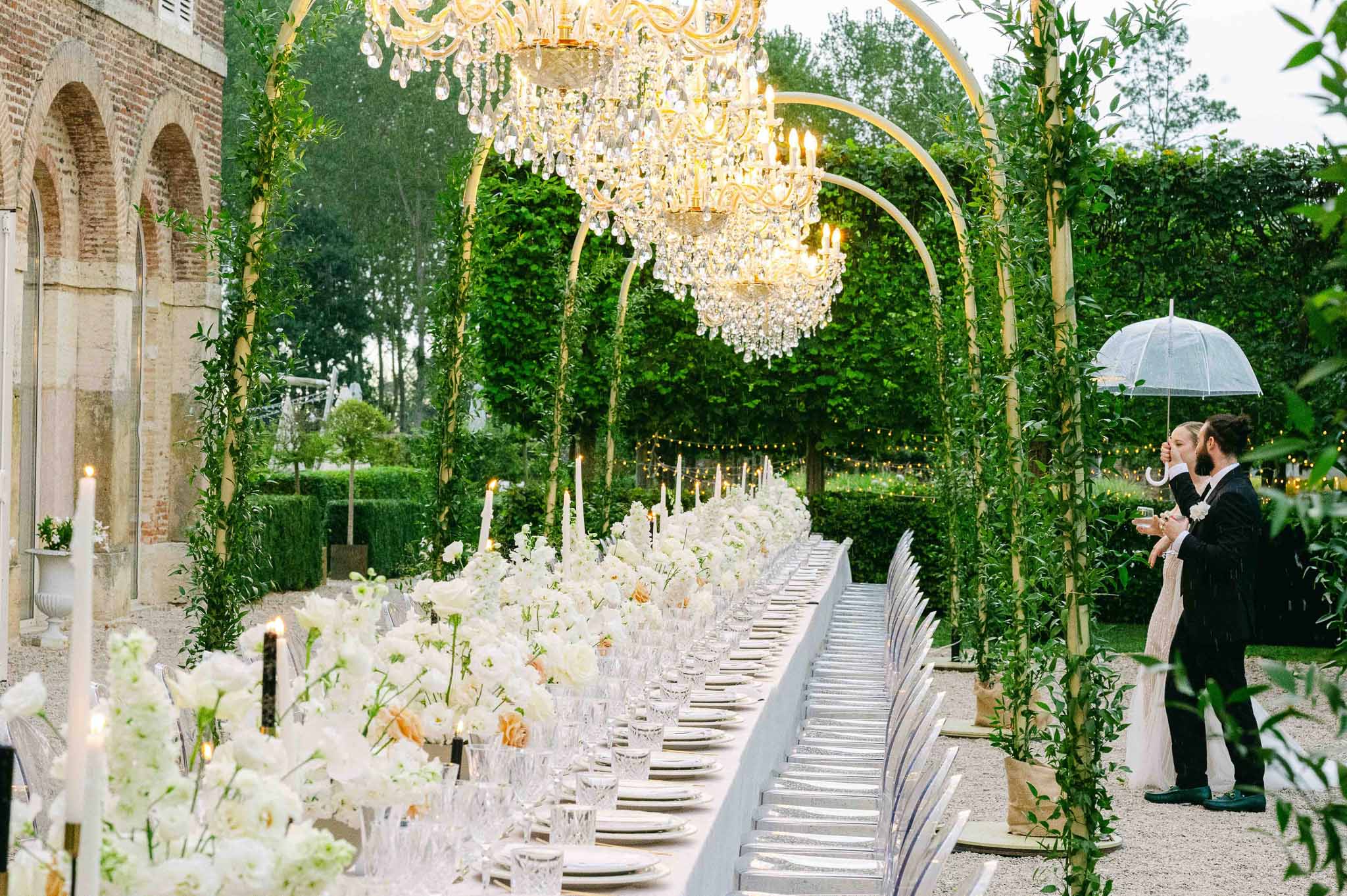 Outdoor reception setup in classical garden courtyard with long banquet table and ivy archways