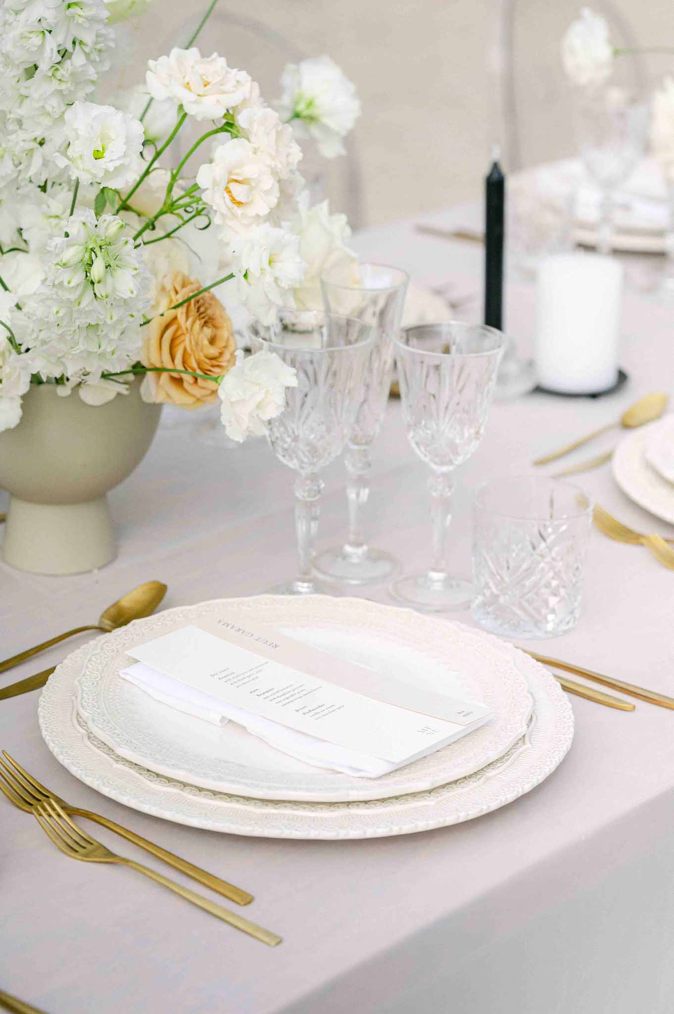 Wedding reception table setting with blush linens, gold flatware, and ivory floral centerpiece at elegant venue