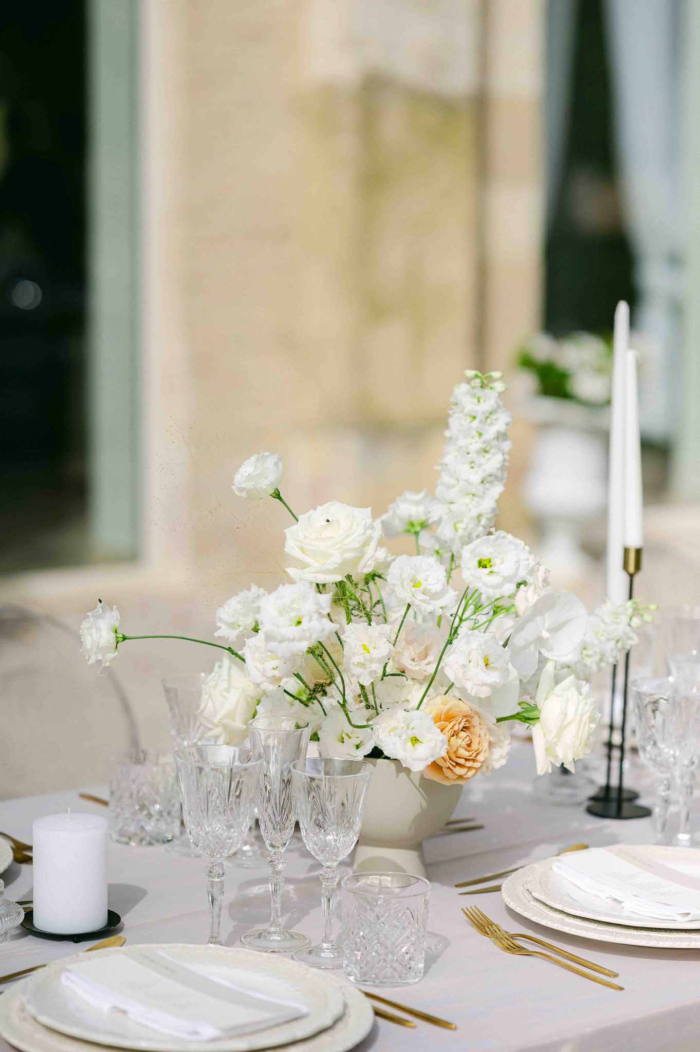 White floral centerpiece and place setting with gold flatware at outdoor wedding reception