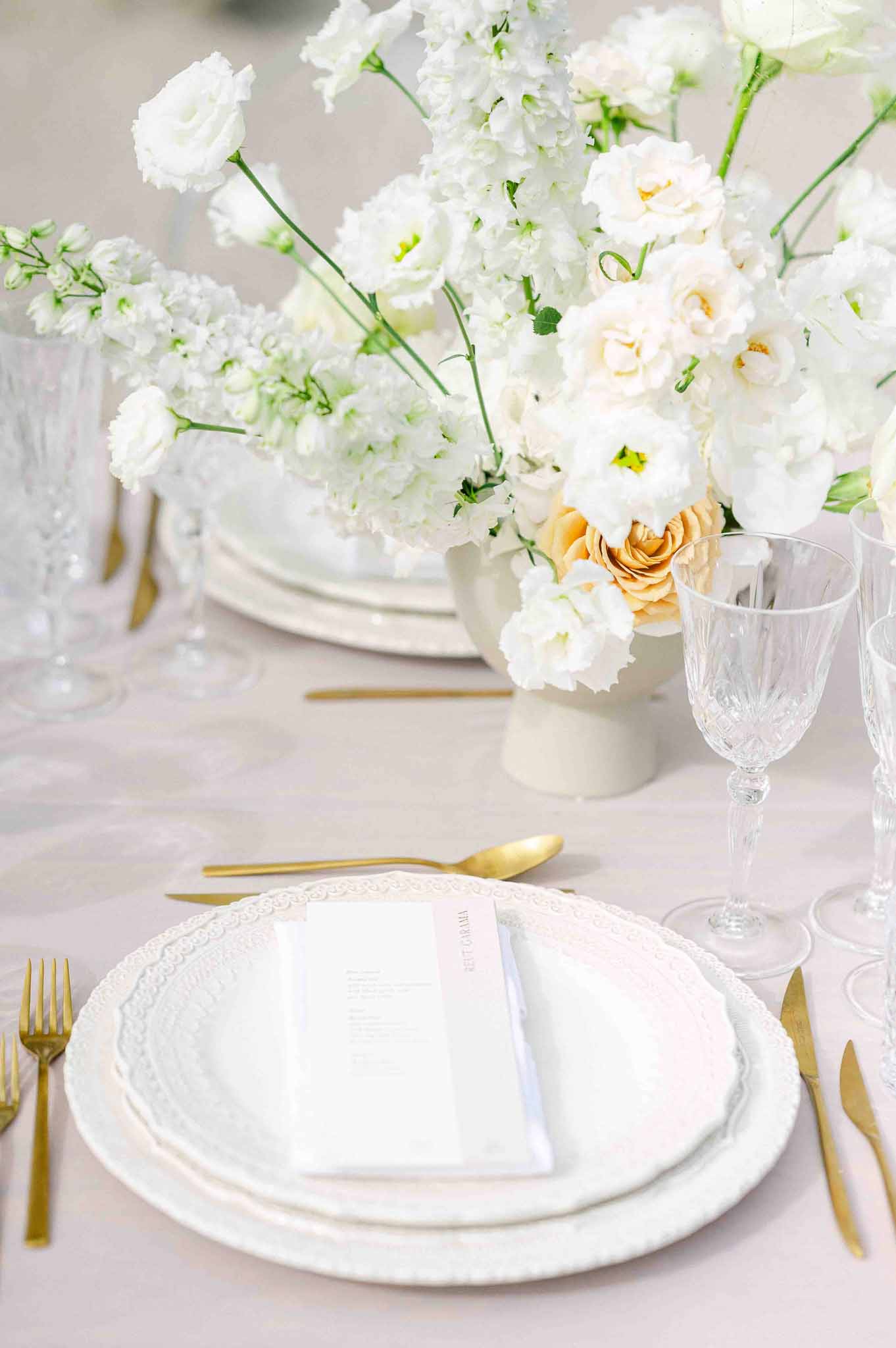 White and gold table setting with floral centerpiece at wedding reception