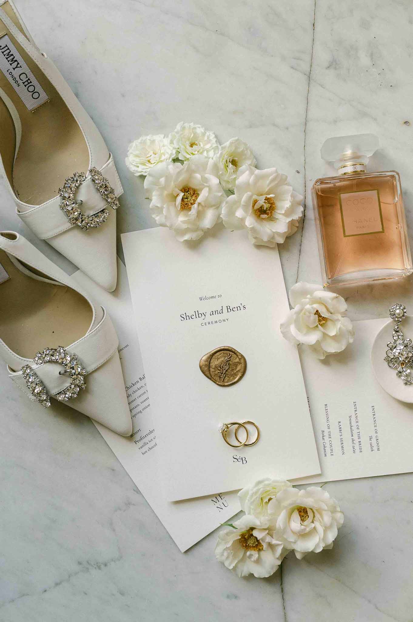 Bridal accessories and wedding stationery flat lay with ivory heels and gold rings on marble surface
