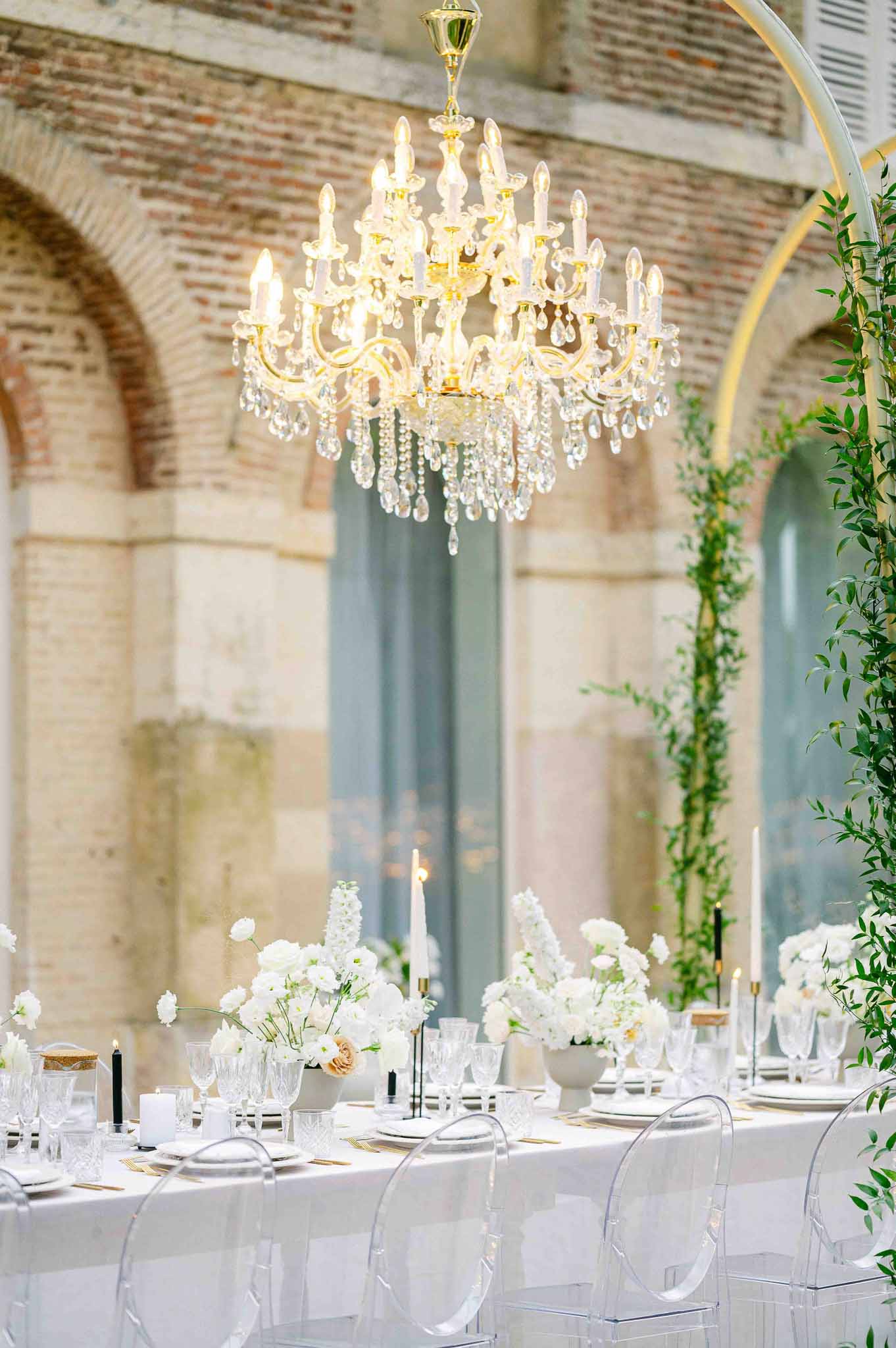 Formal reception dining setup with crystal chandelier in historic stone venue with exposed brick archways