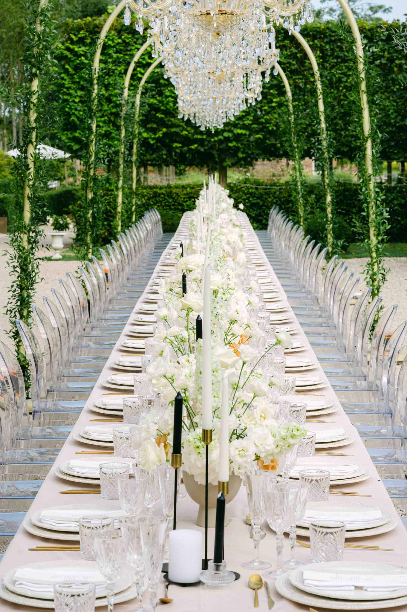 Elegant outdoor reception table setting with floral centerpiece and crystal chandelier in formal garden