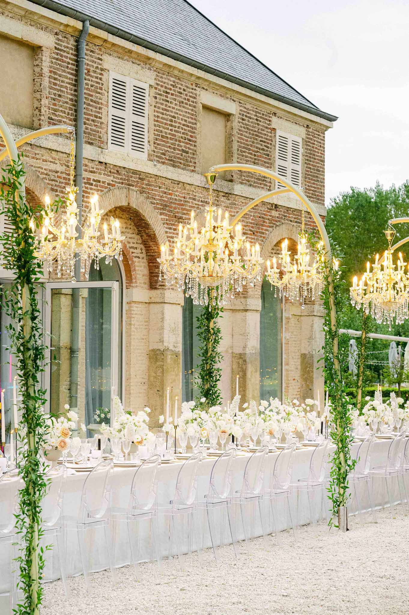 Reception setup with crystal chandeliers and white florals on historic brick building courtyard terrace