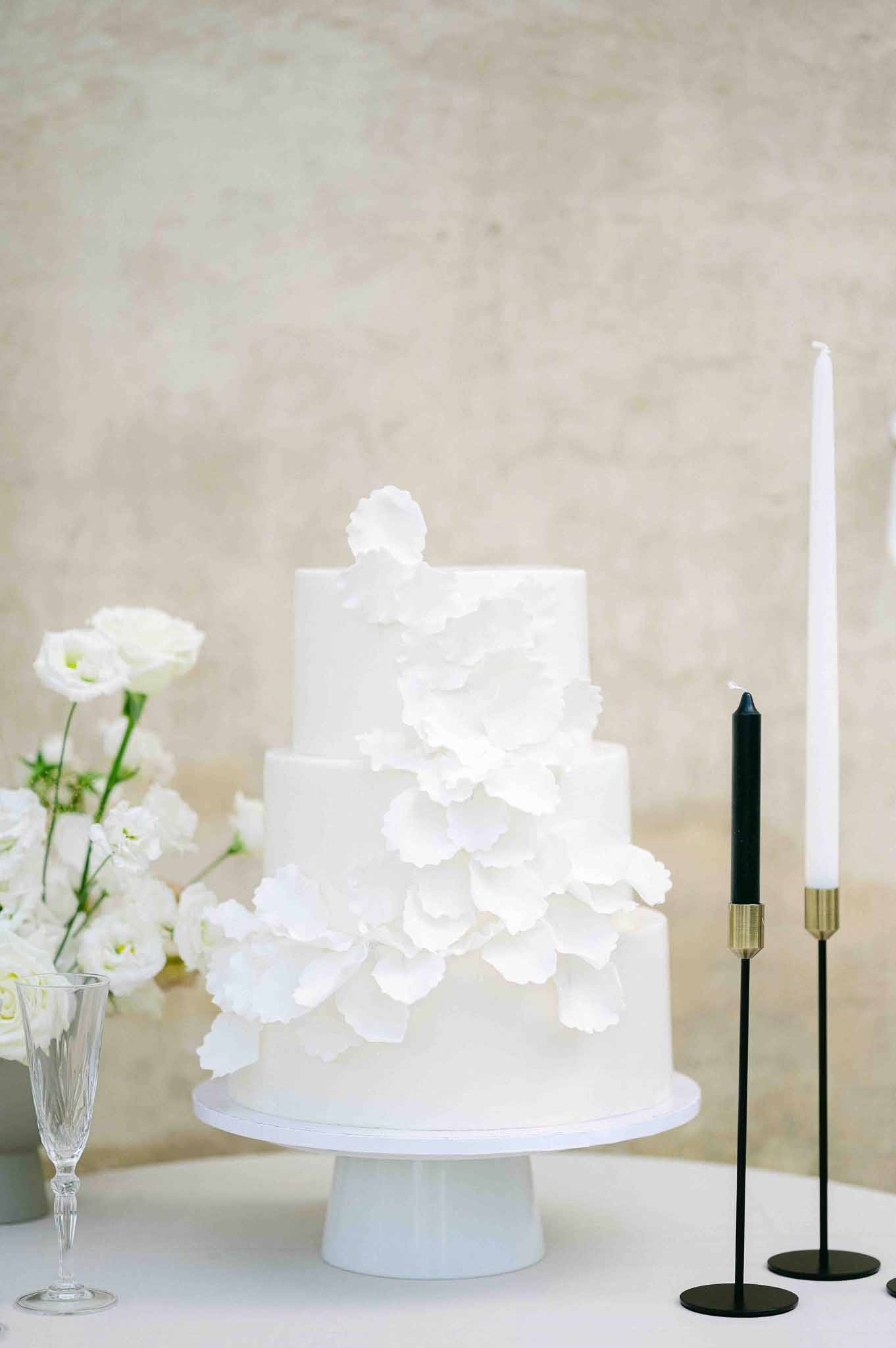 White three-tier wedding cake with sugar flowers and black candlesticks on styled table setting