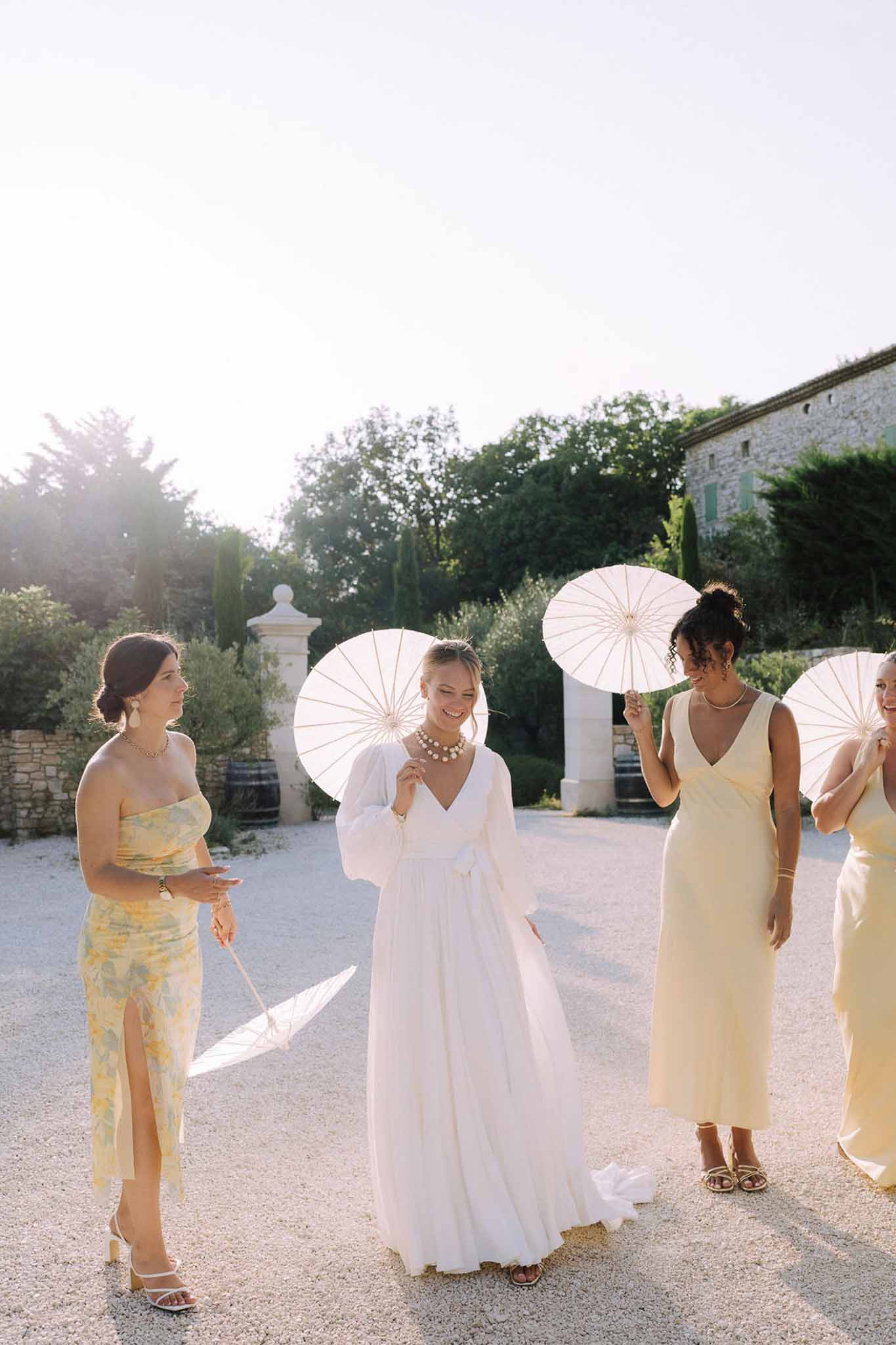Bride and bridesmaids with parasols in Mediterranean stone courtyard during golden hour portrait session