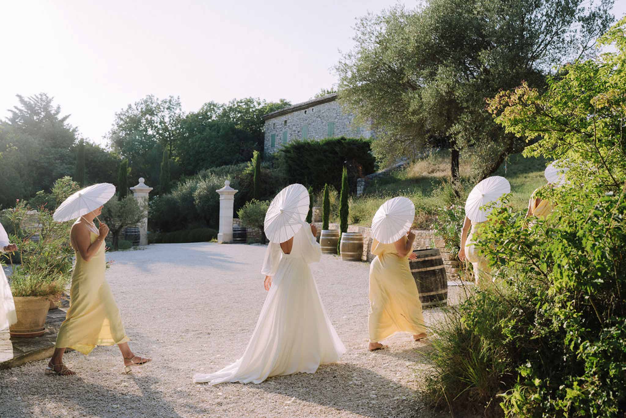 Bride and bridesmaids with parasols walking through stone villa courtyard during wedding processional