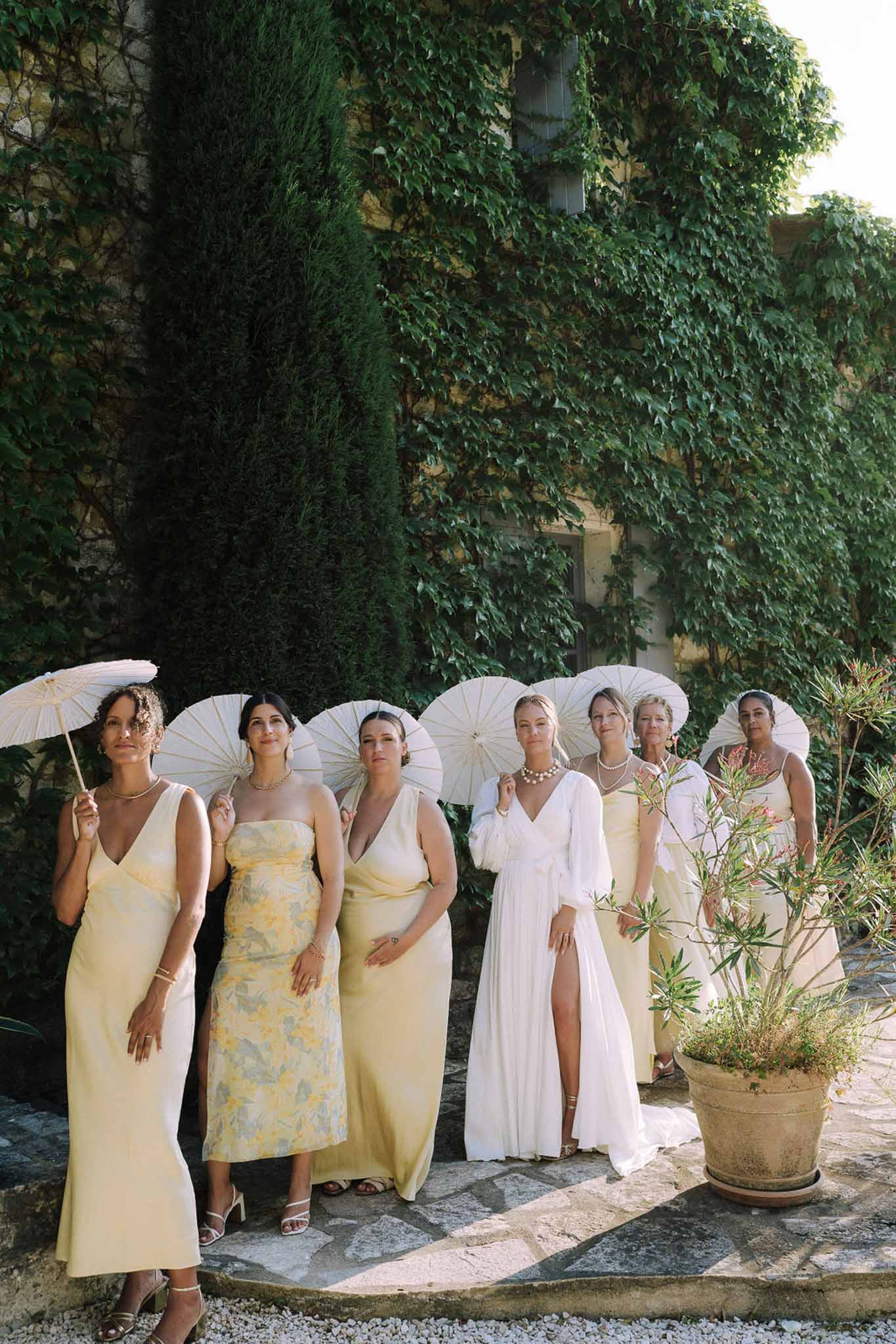 Bridal party in pastel dresses with parasols at stone courtyard
