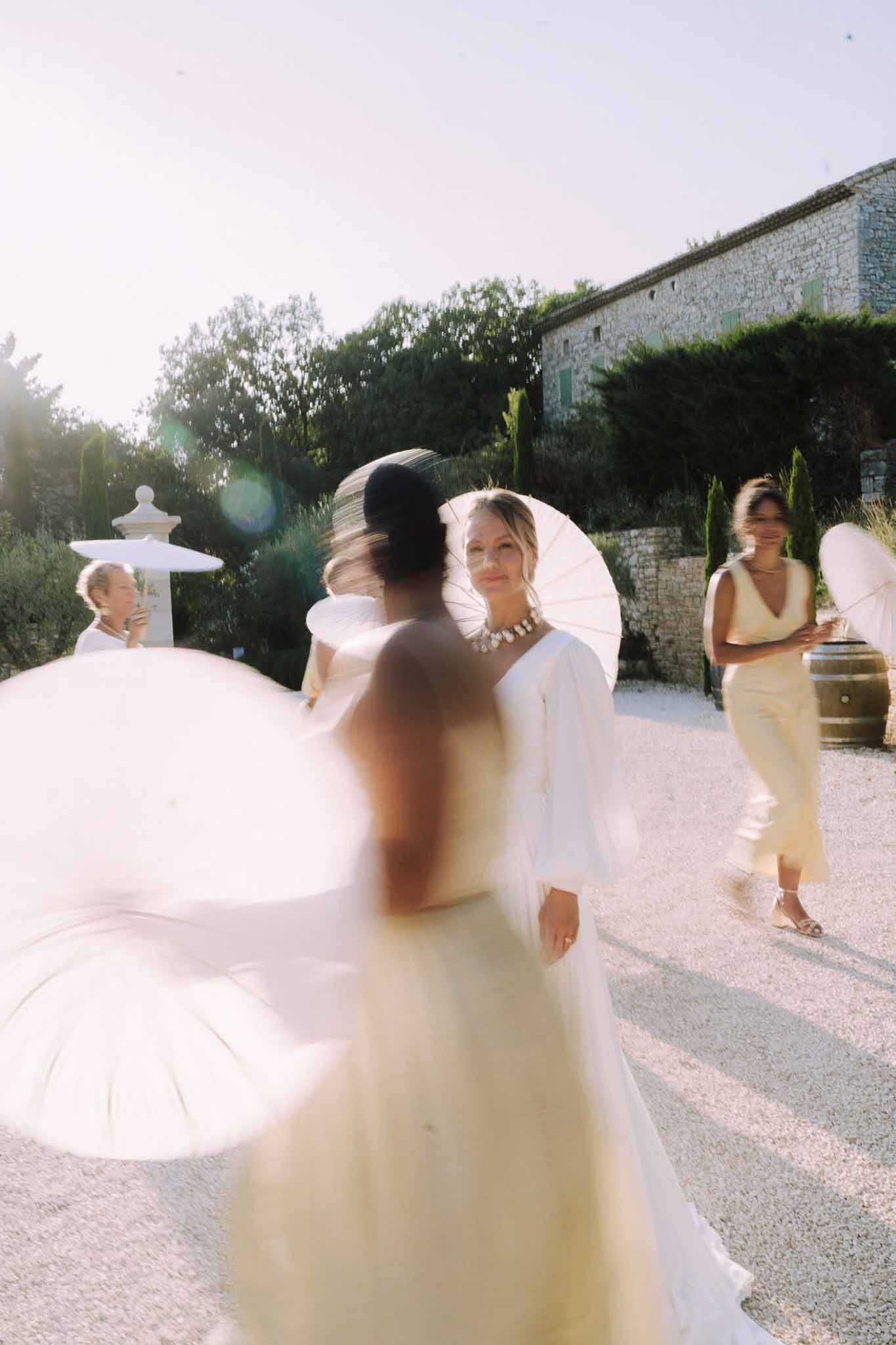 Bride with white parasol interacting with guests in stone courtyard during wedding reception