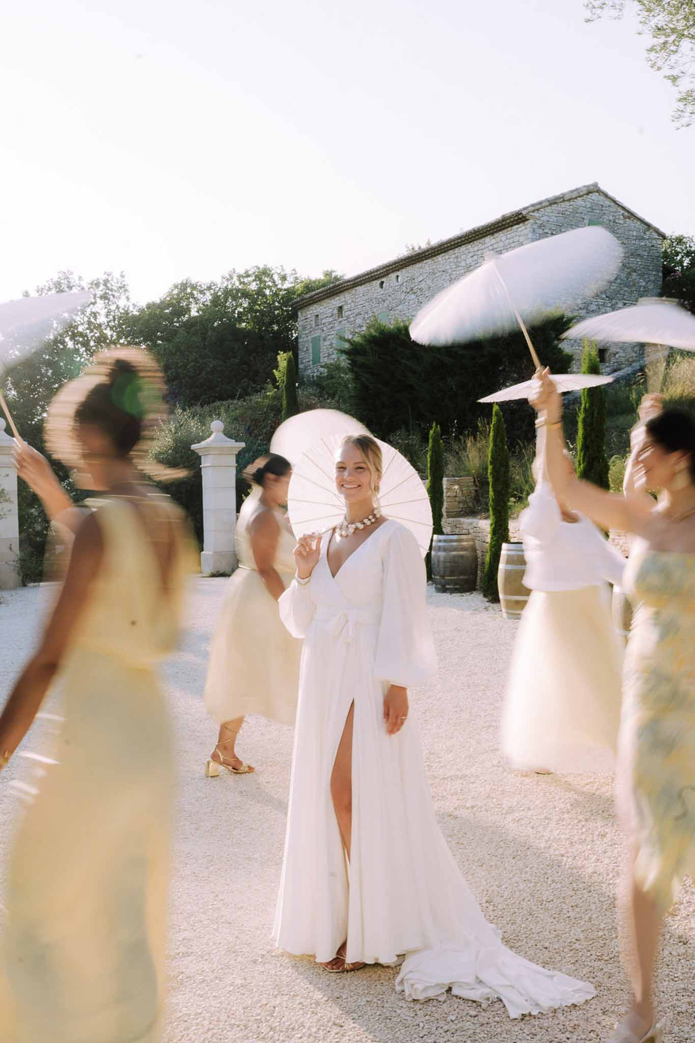 Bride with bridesmaids holding parasols in stone courtyard at Mediterranean venue