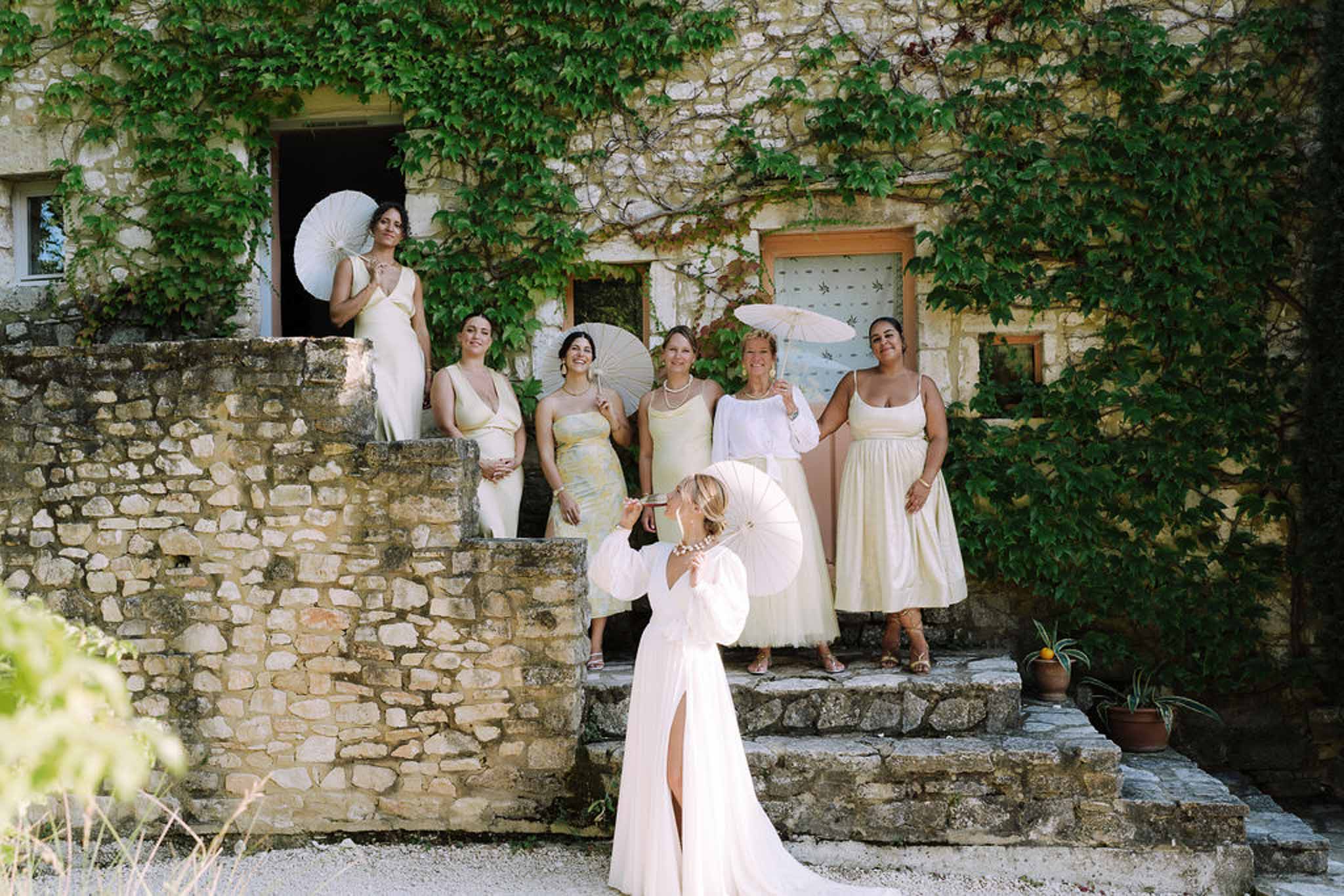 Bride and bridesmaids with white parasols at historic stone courtyard wedding venue
