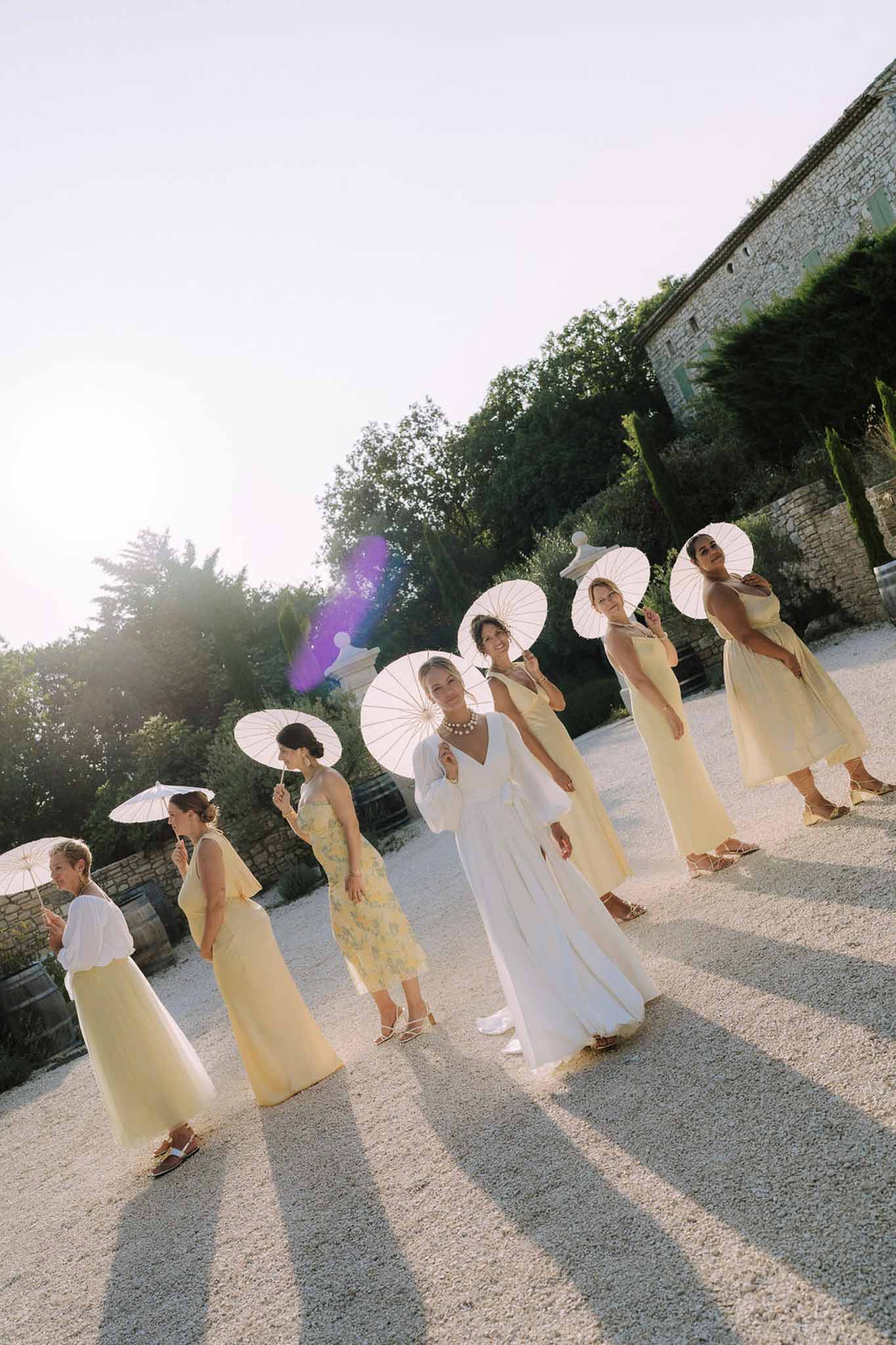 Bride and bridesmaids with white umbrellas in stone courtyard at French chateau wedding