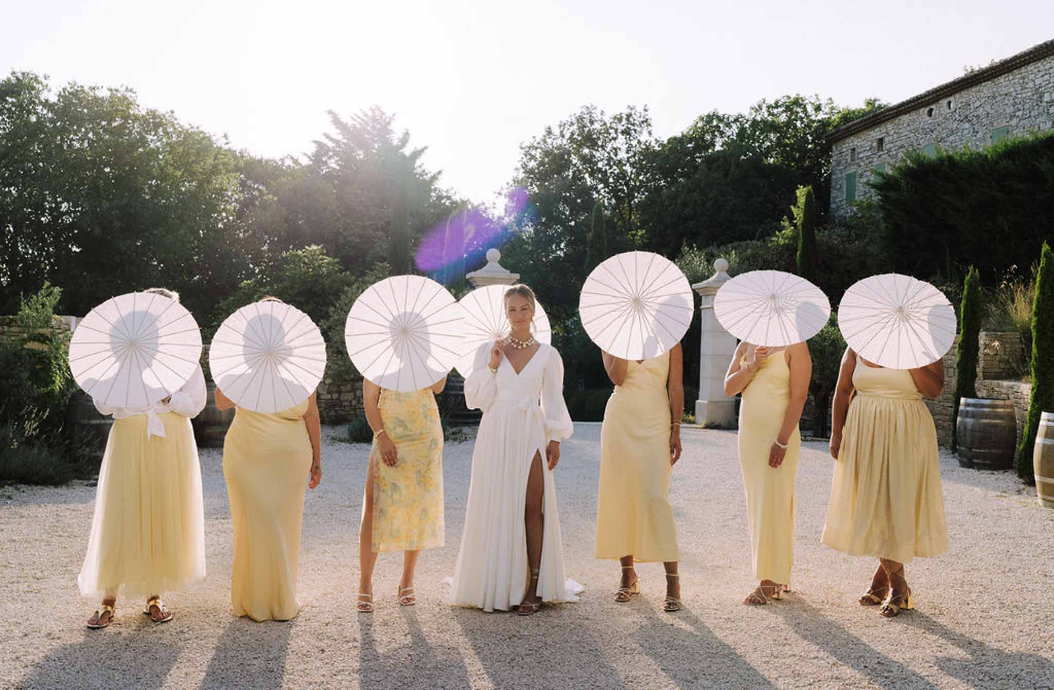 Bride and bridesmaids with white parasols in courtyard garden setting