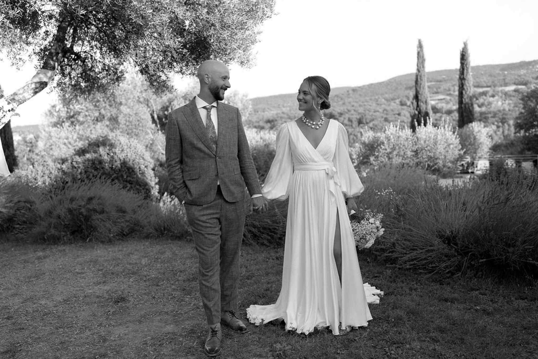 Bride and groom walking hand-in-hand through Mediterranean garden with olive trees