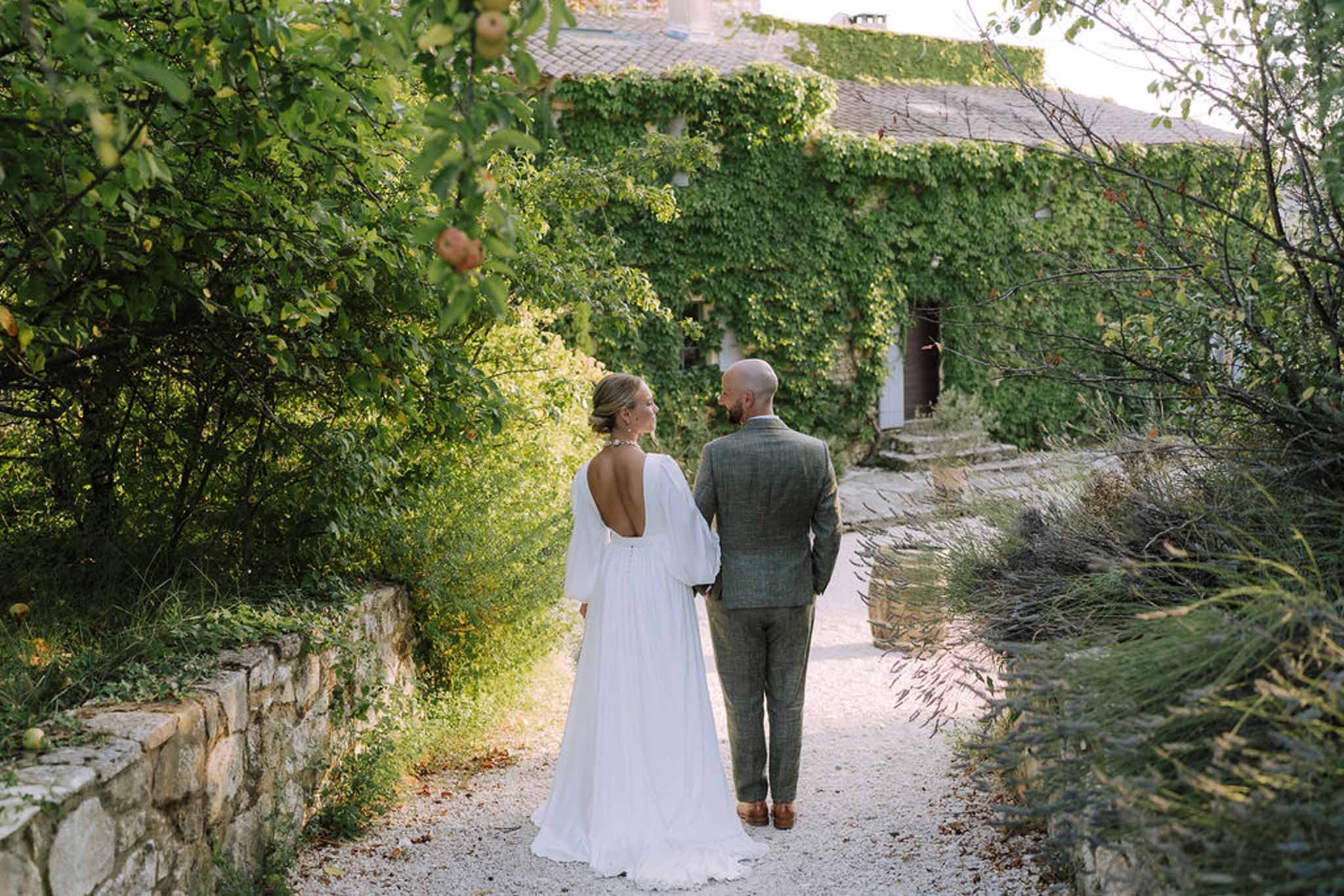 Bride and groom walking down ivy-lined stone pathway at historic countryside estate