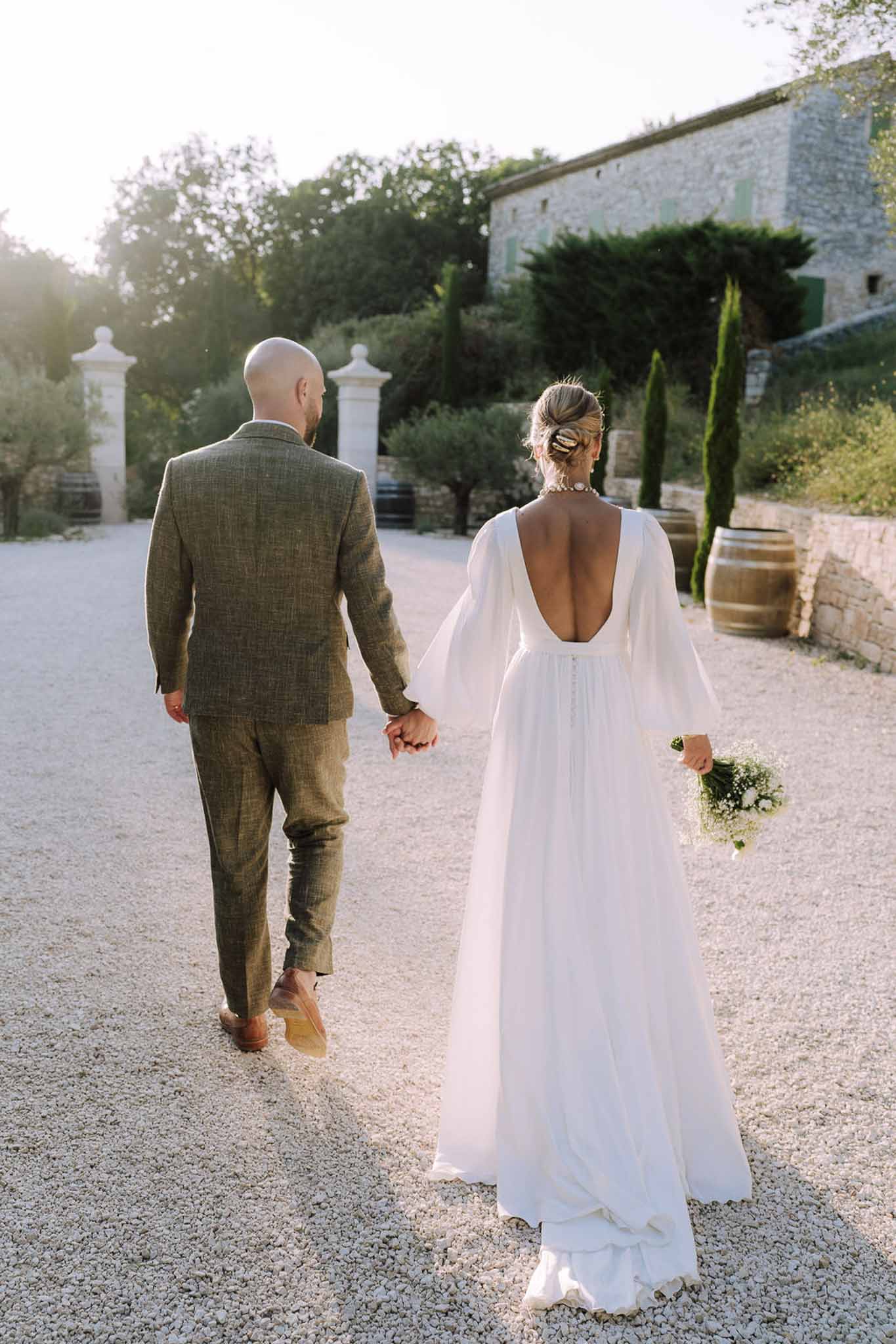 Bride and groom walking hand-in-hand through stone courtyard during golden hour portrait session