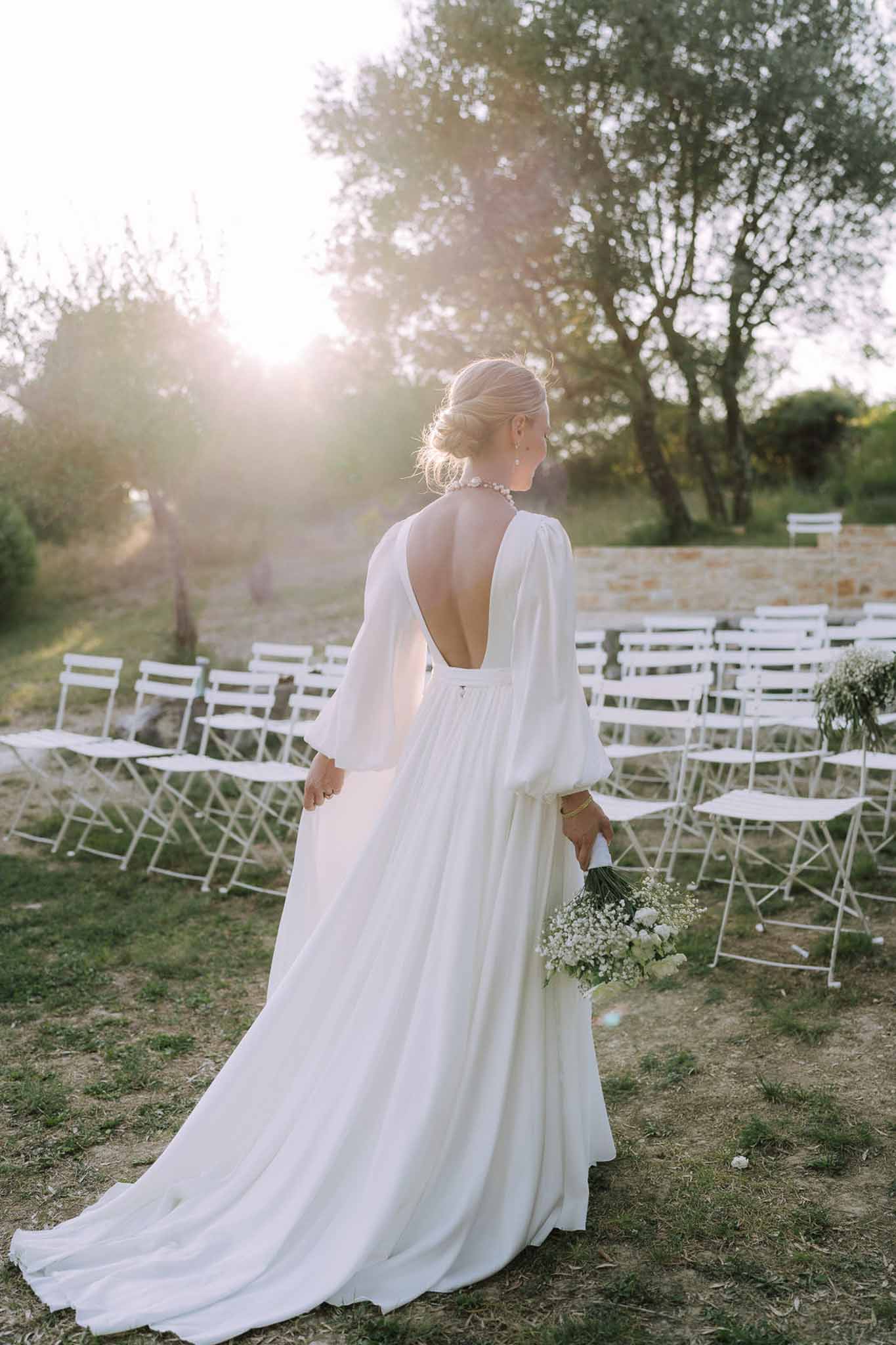 Bride in ivory gown with chapel train standing in outdoor ceremony space with white chairs