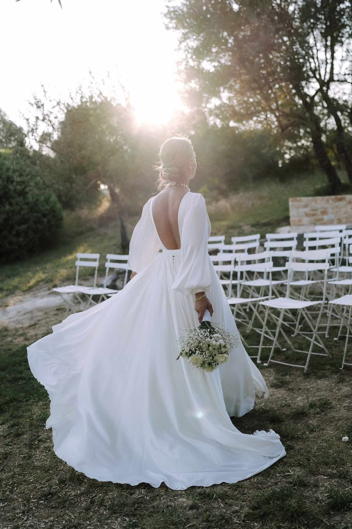 Bride in ivory wedding dress holding white bouquet in outdoor garden ceremony space