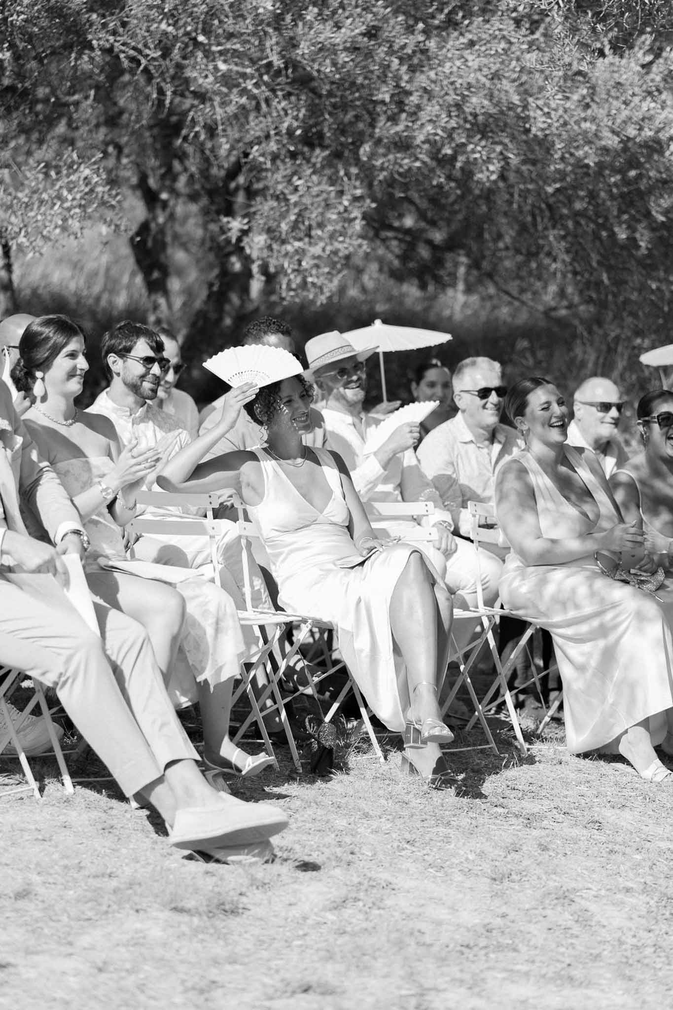 Wedding guests seated in folding chairs watching outdoor ceremony or reception moment