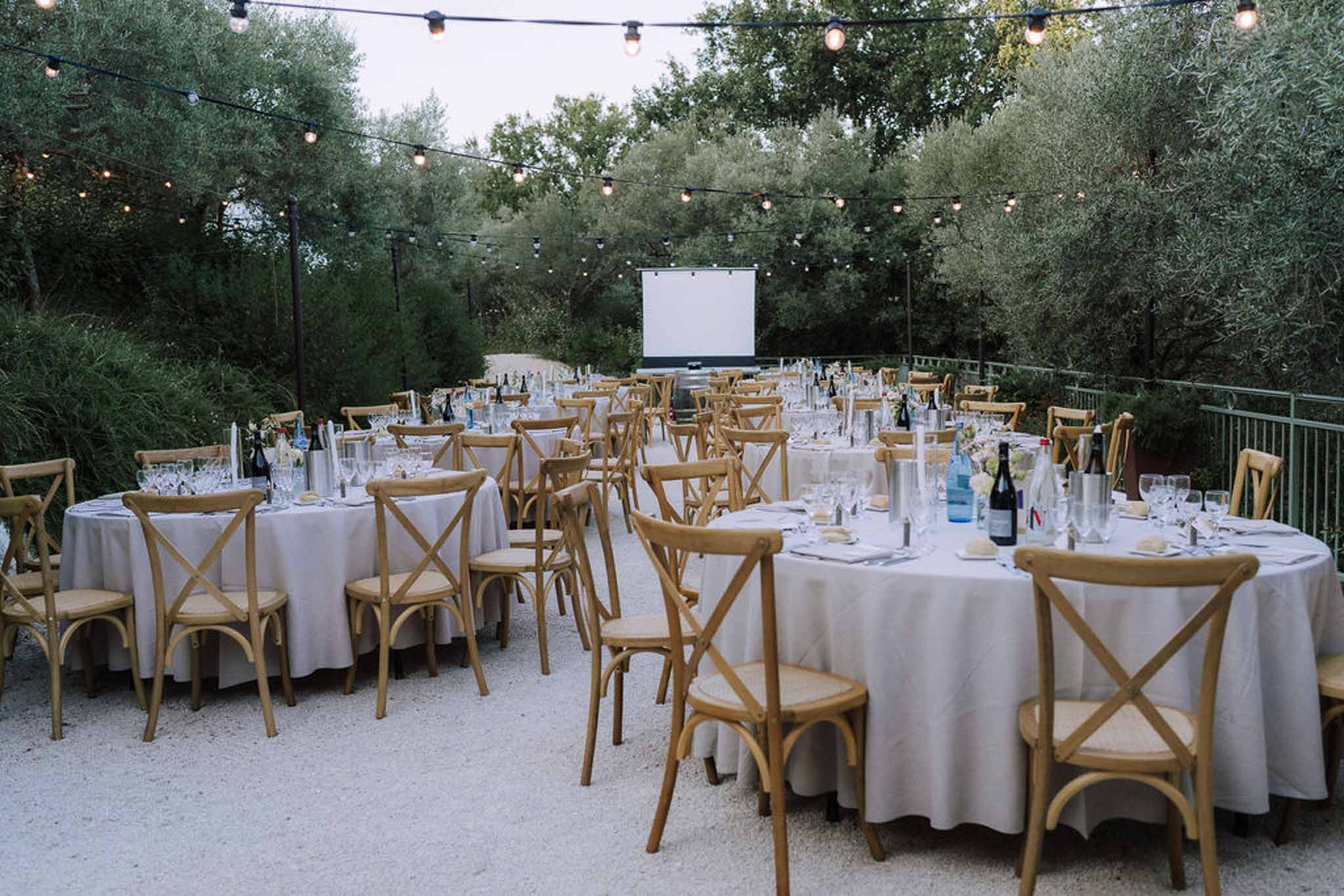 Outdoor reception setup with round tables in olive grove garden venue with string lighting