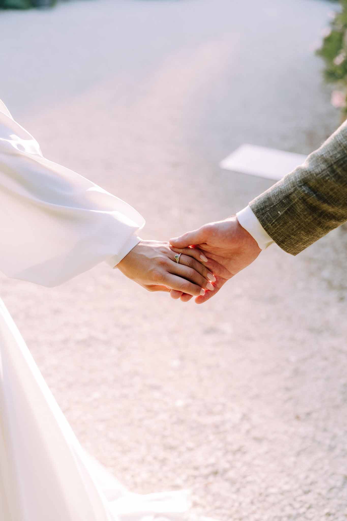 Bride and groom's joined hands showing wedding rings at outdoor waterfront ceremony