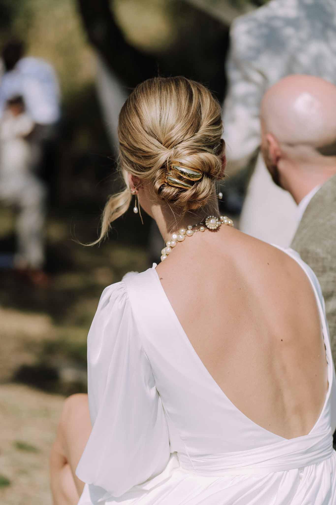 Bride's low twisted updo and pearl jewelry during outdoor wedding ceremony