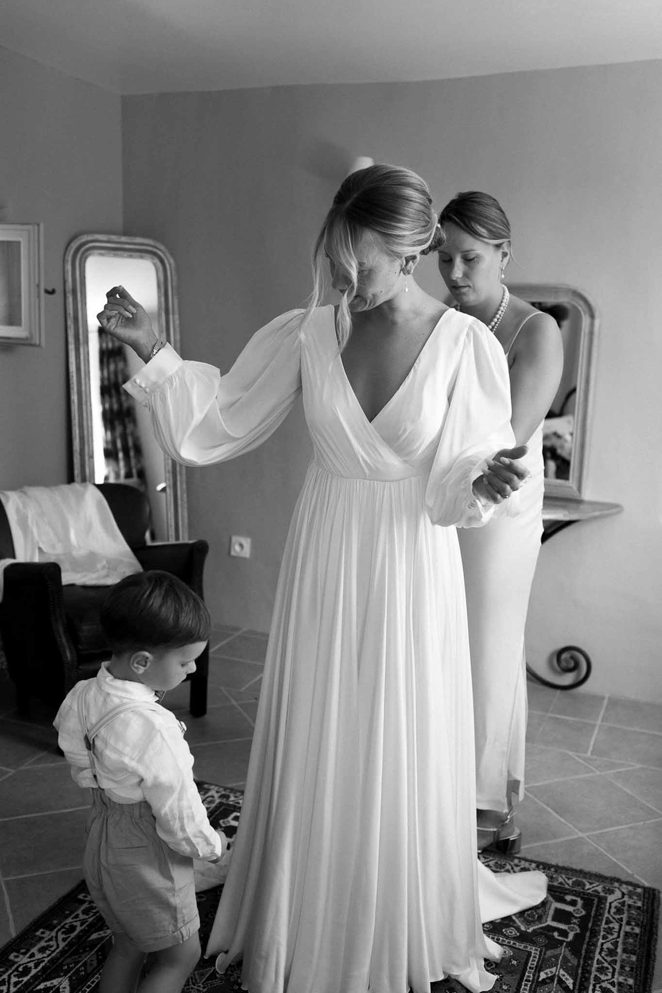 Bride getting ready with assistance from family member and child in bridal suite with ornate mirror