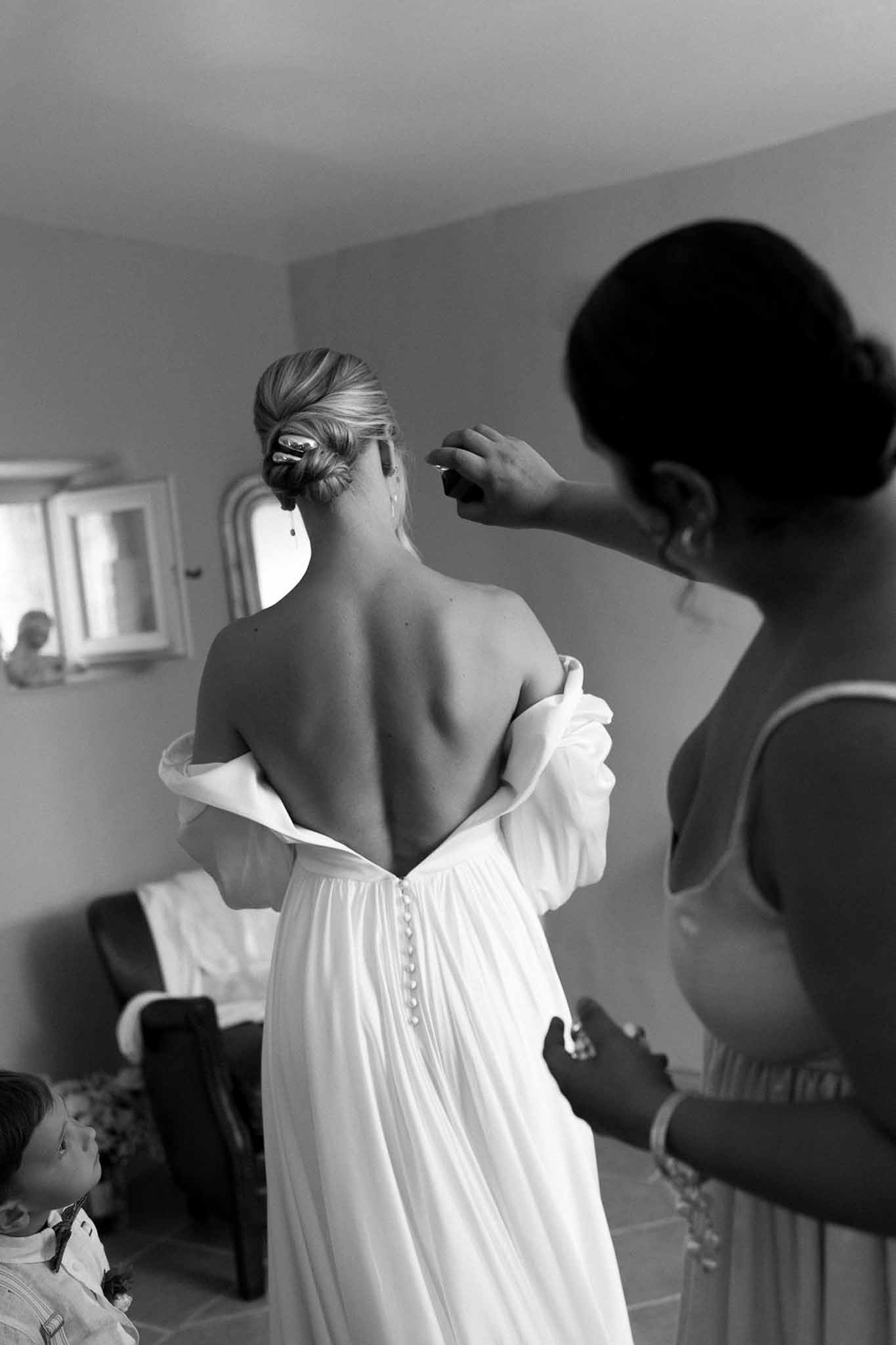 Bride having wedding dress buttoned up during getting ready preparations in minimalist bedroom