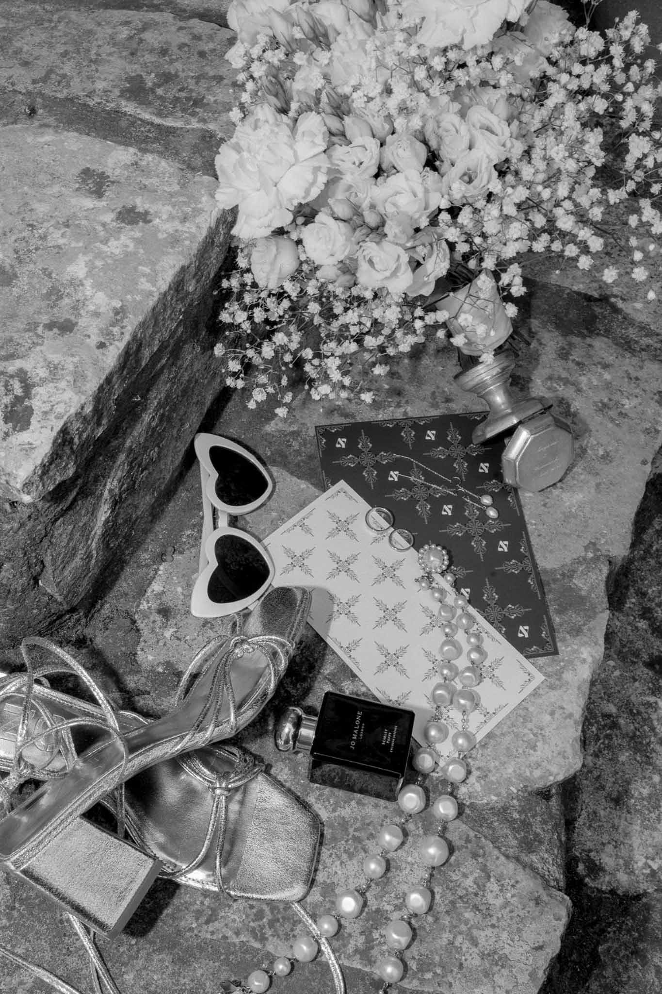 Black and white flat lay of bridal accessories and bouquet on stone surface