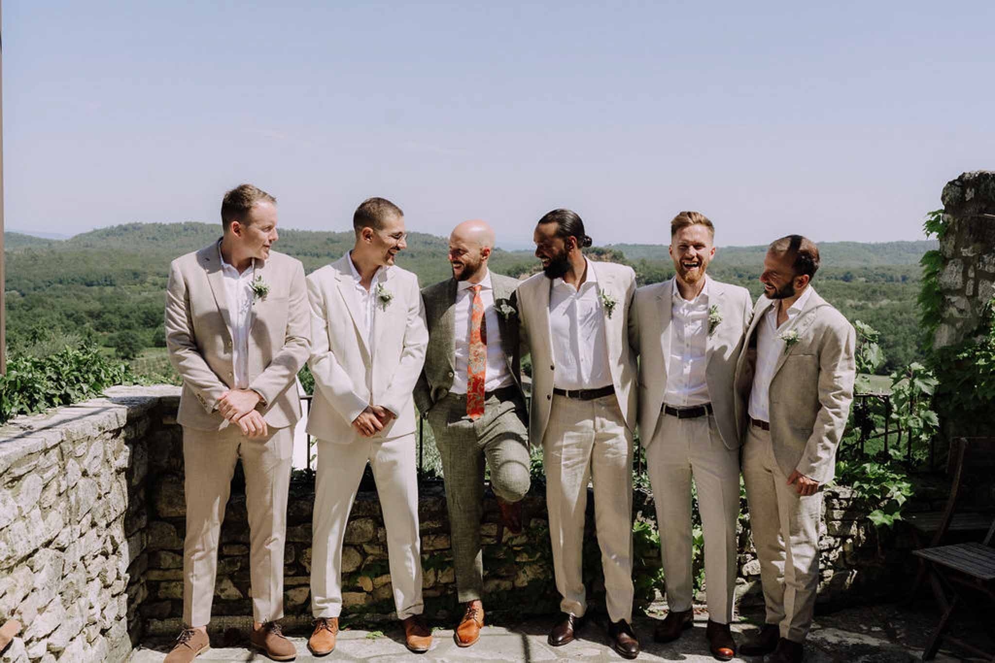 Groom and groomsmen in linen suits on outdoor terrace overlooking valley at countryside wedding venue