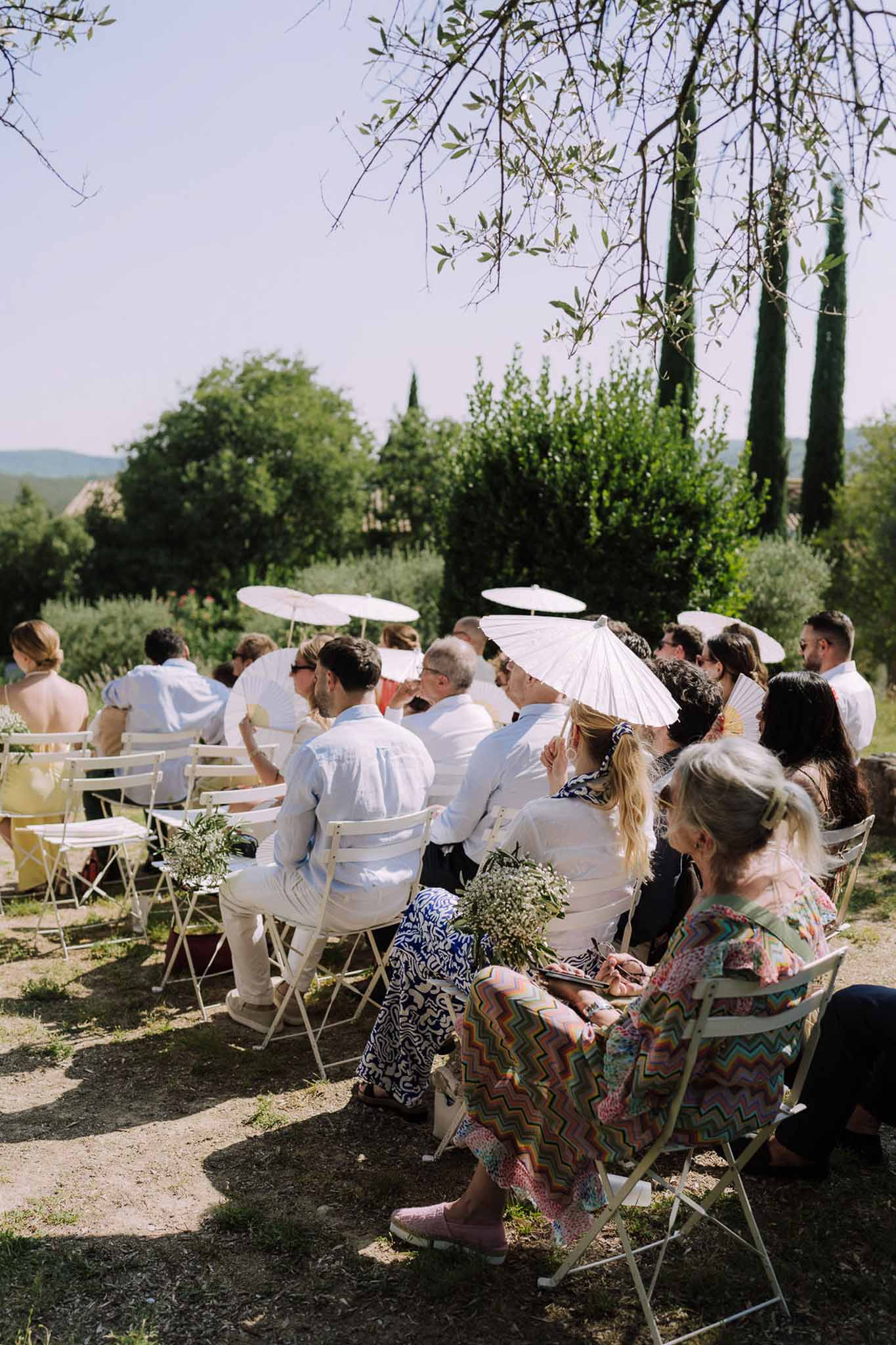 Outdoor cocktail reception with guests seated in garden chairs in Tuscan countryside setting