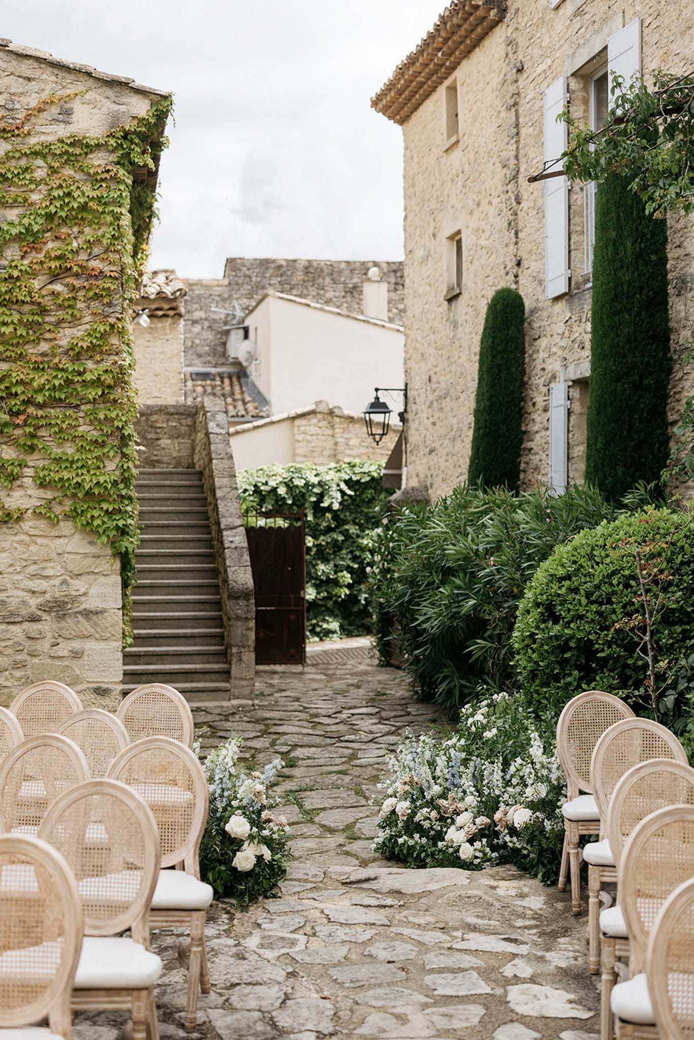 Wedding ceremony setup in historic stone courtyard with natural wood chairs and white floral arrangements