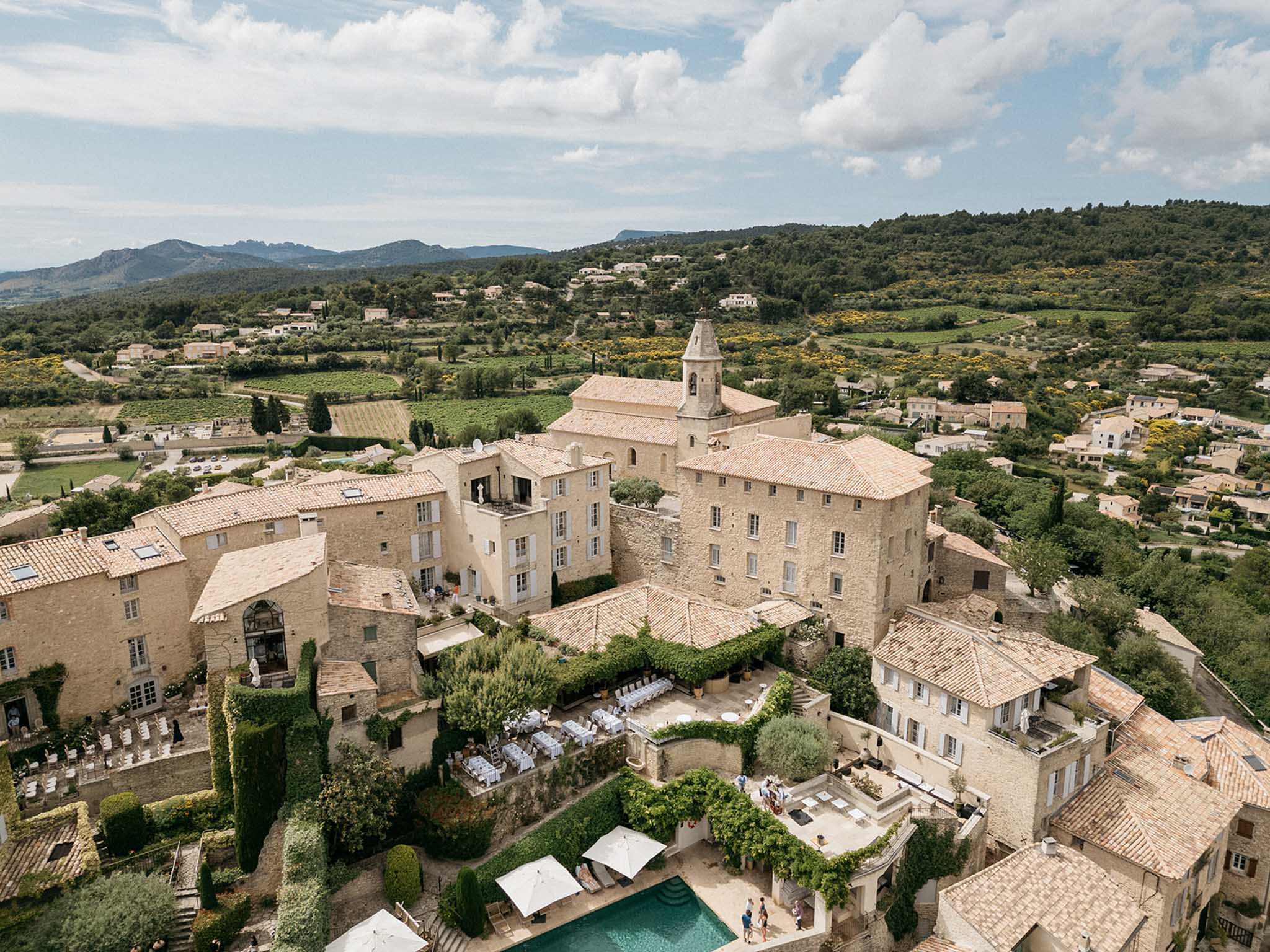 Aerial view of medieval stone château with reception setup and pool in Provence countryside