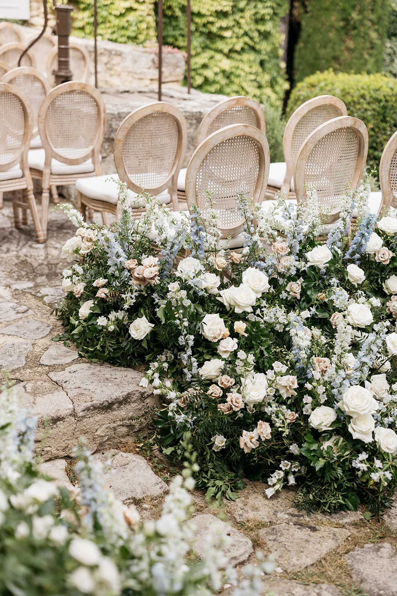 Outdoor ceremony aisle with floral arrangements and cane-back chairs in European garden courtyard