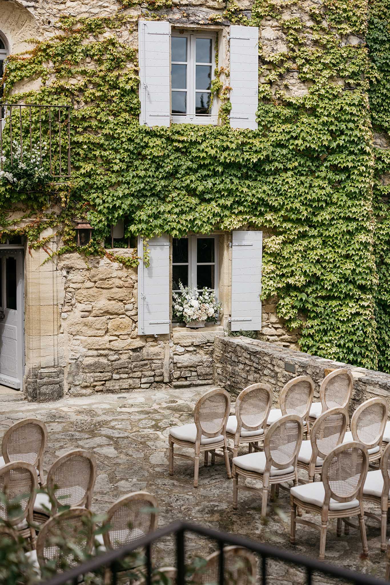 French stone courtyard ceremony setup with wooden chairs facing ivy-covered building