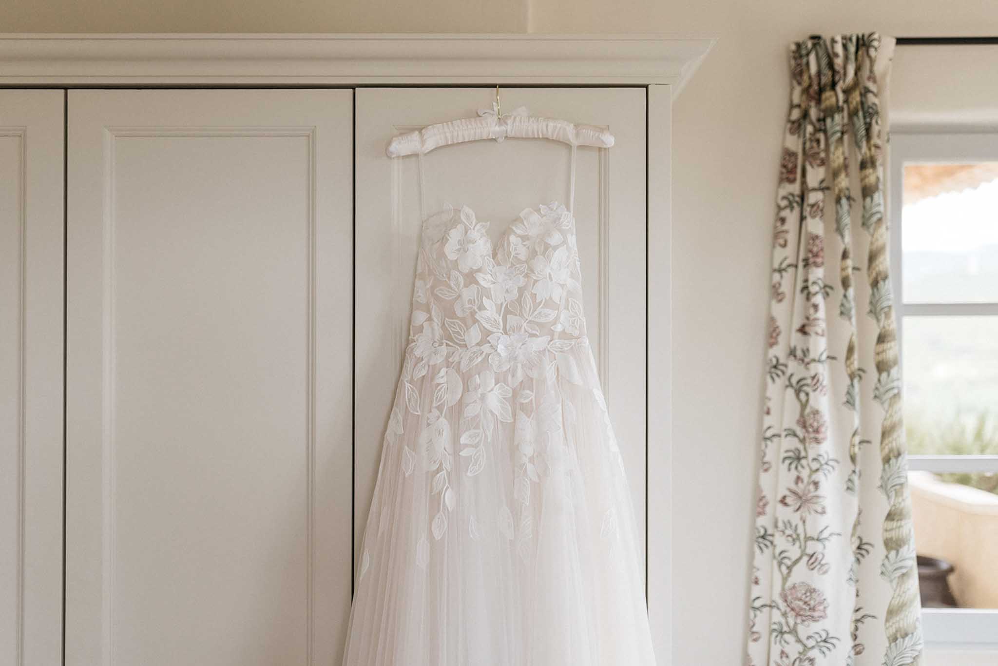 Bride's wedding dress hanging on hanger in getting ready room with classic interior