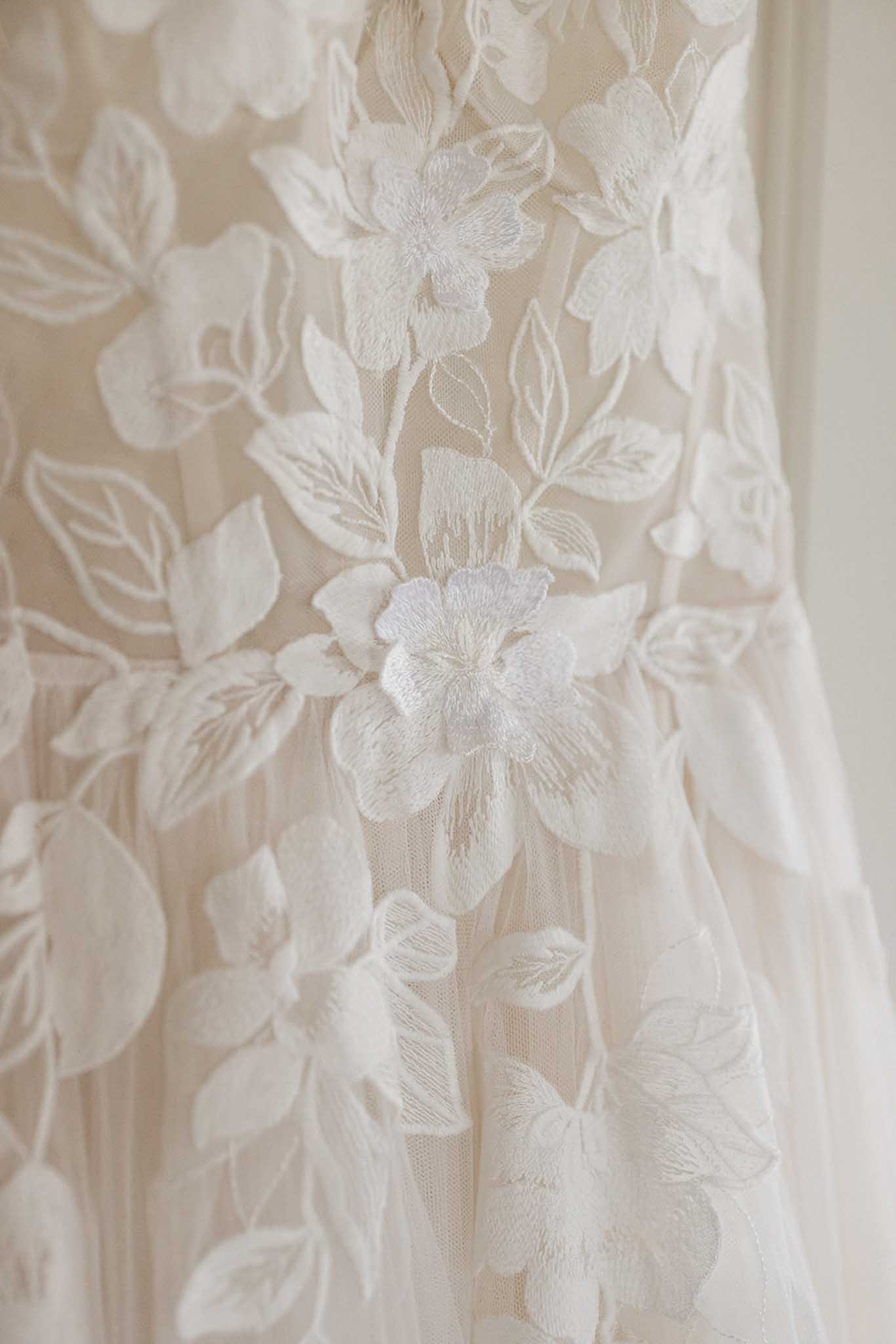 Close-up of ivory embroidered floral details on wedding dress fabric showing intricate botanical needlework