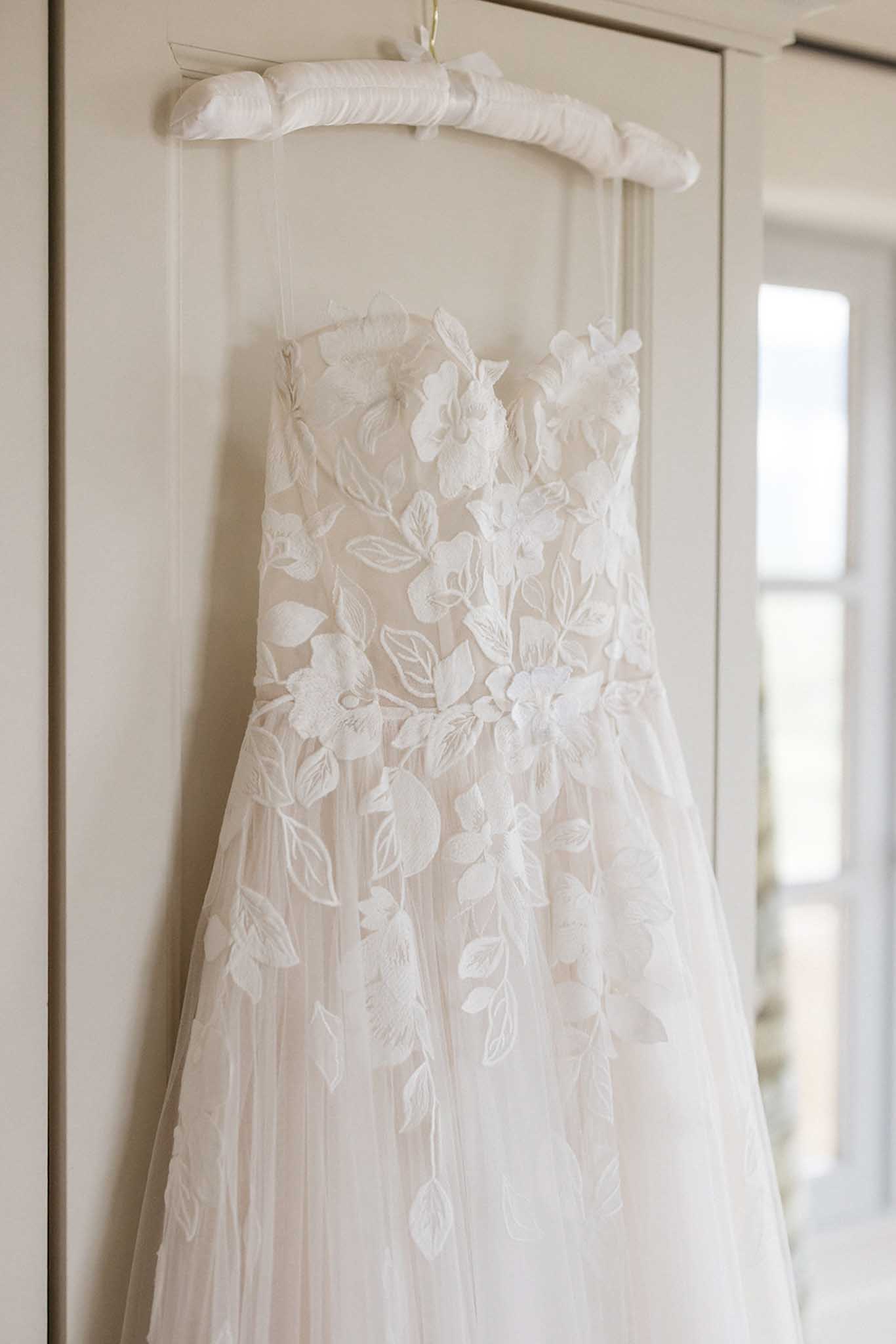 Wedding dress with floral appliqués hanging on hanger in bridal suite