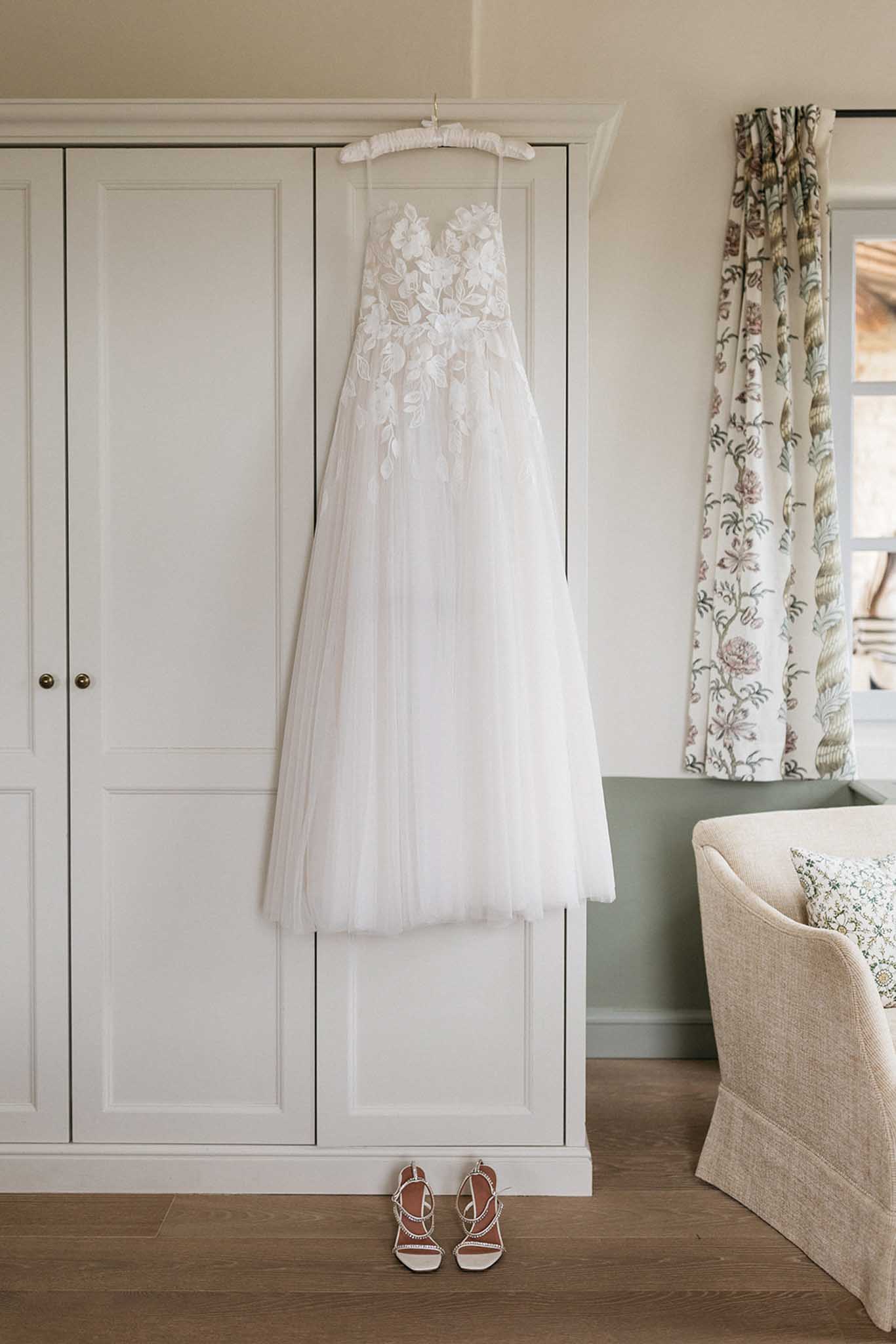 Ivory ball gown with floral appliqués and tan sandals hanging in bridal preparation room