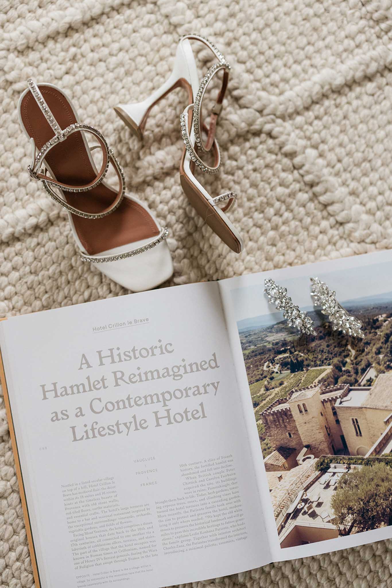 Bridal shoes and crystal earrings arranged with wedding magazine featuring French château venue