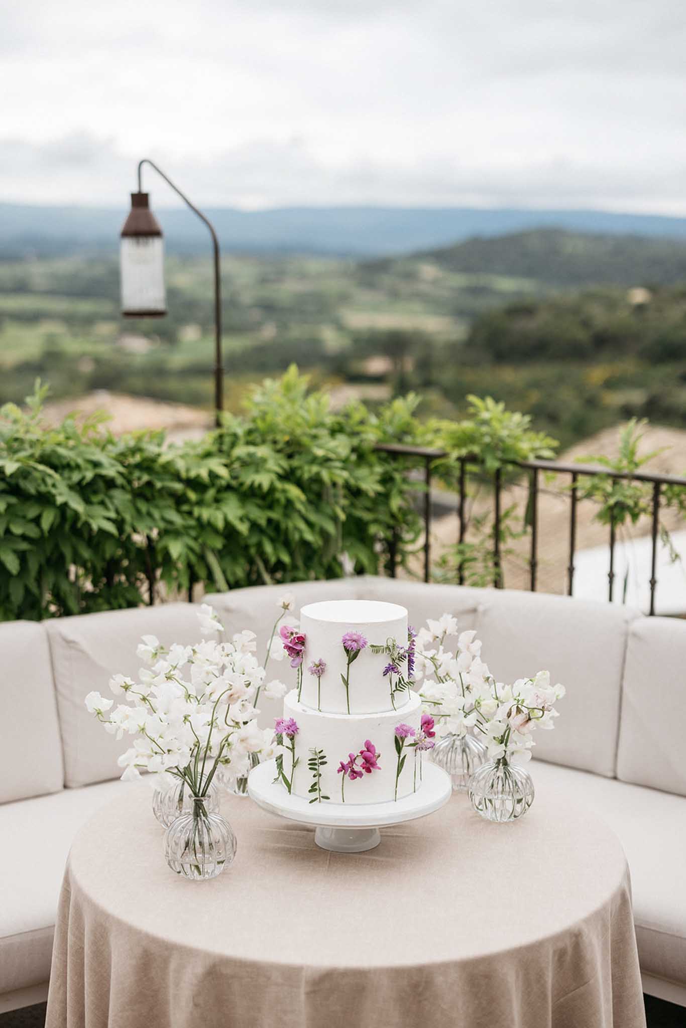 Two-tier wedding cake with floral details on outdoor terrace reception table