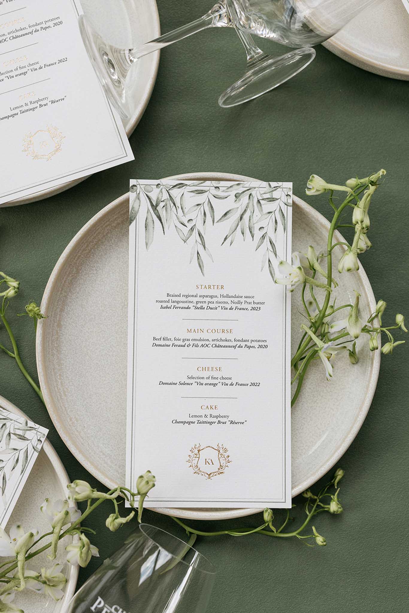 Wedding reception place setting flat lay with menu card and white flowers on green tablecloth