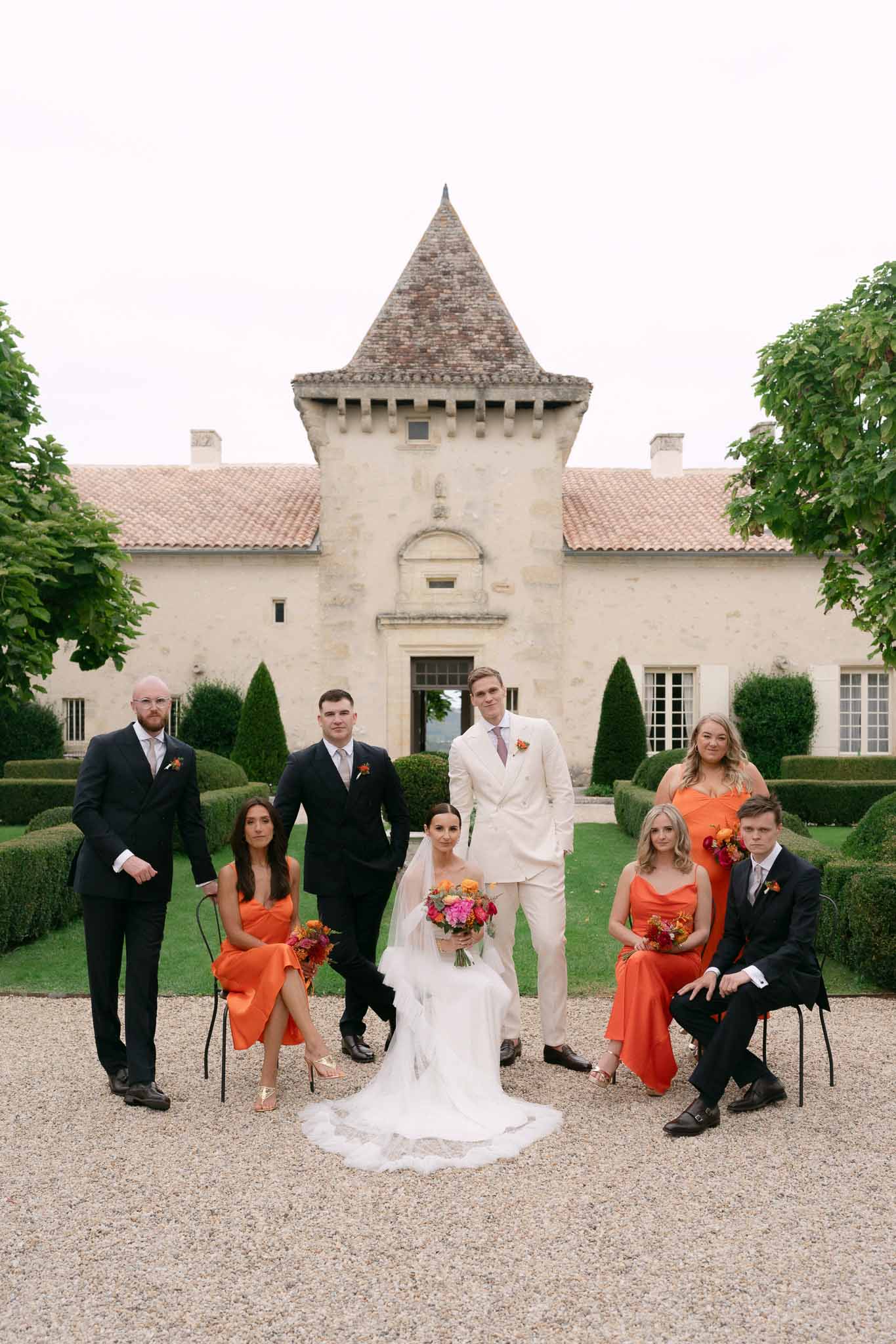 Bridal party with tangerine bridesmaids and navy groomsmen at chateau with topiary hedges